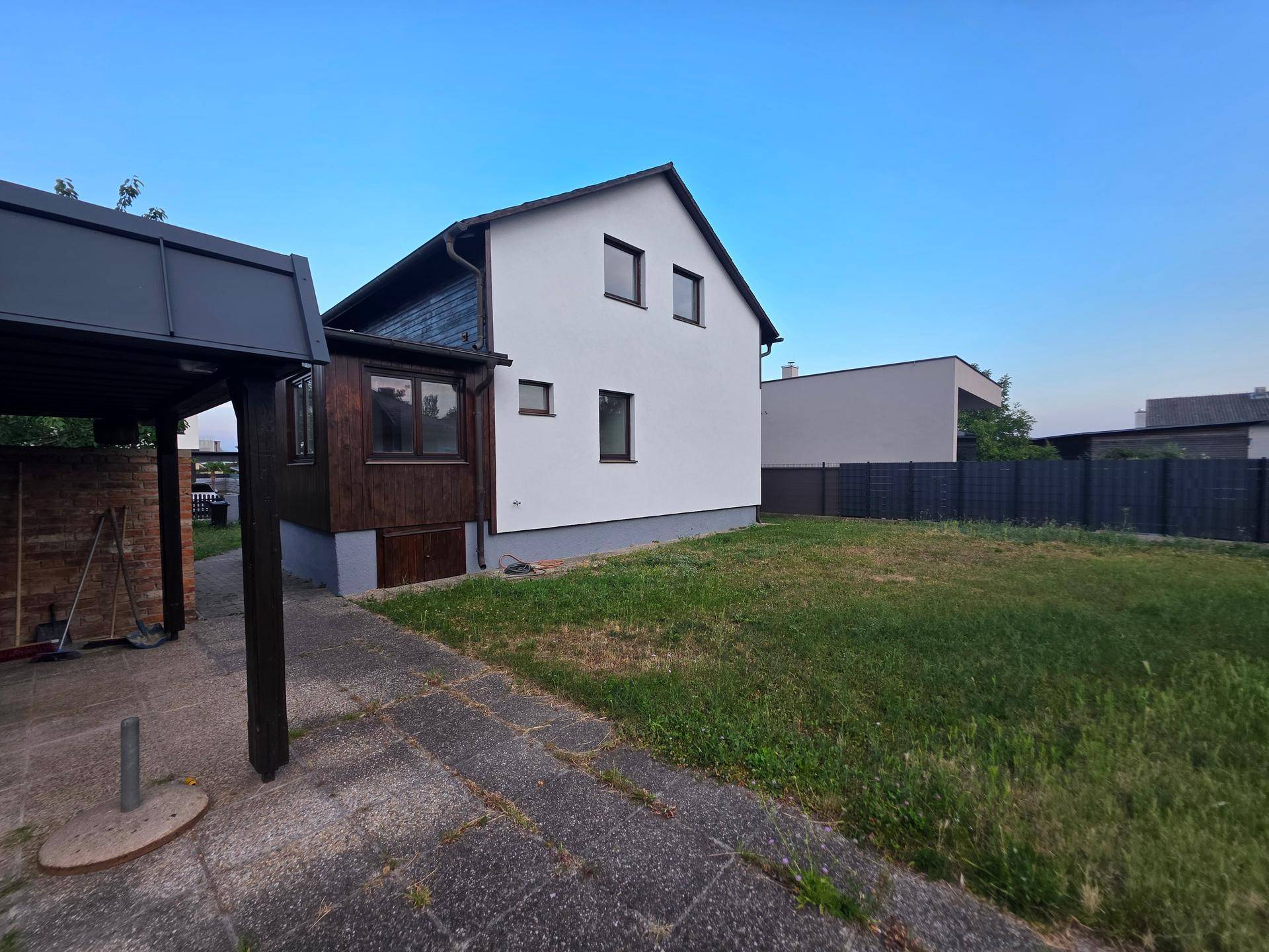 Seitenansicht des Hauses mit weißer Fassade, Holzverkleidung und angrenzendem Garten.