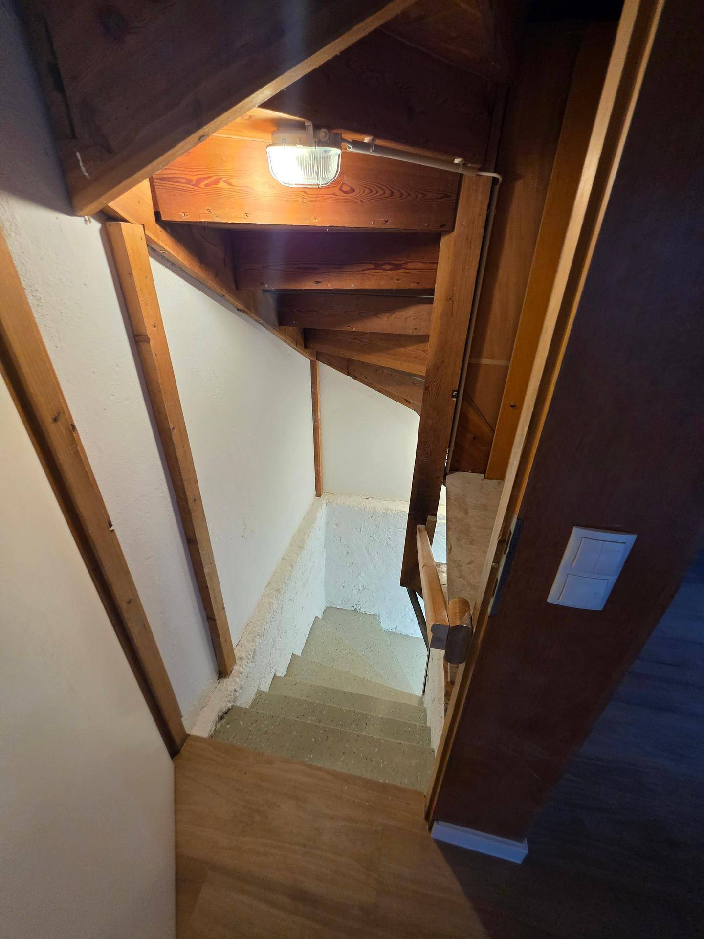 Holztreppe führt hinunter in den Kellerbereich, mit sichtbaren Holzbalken.