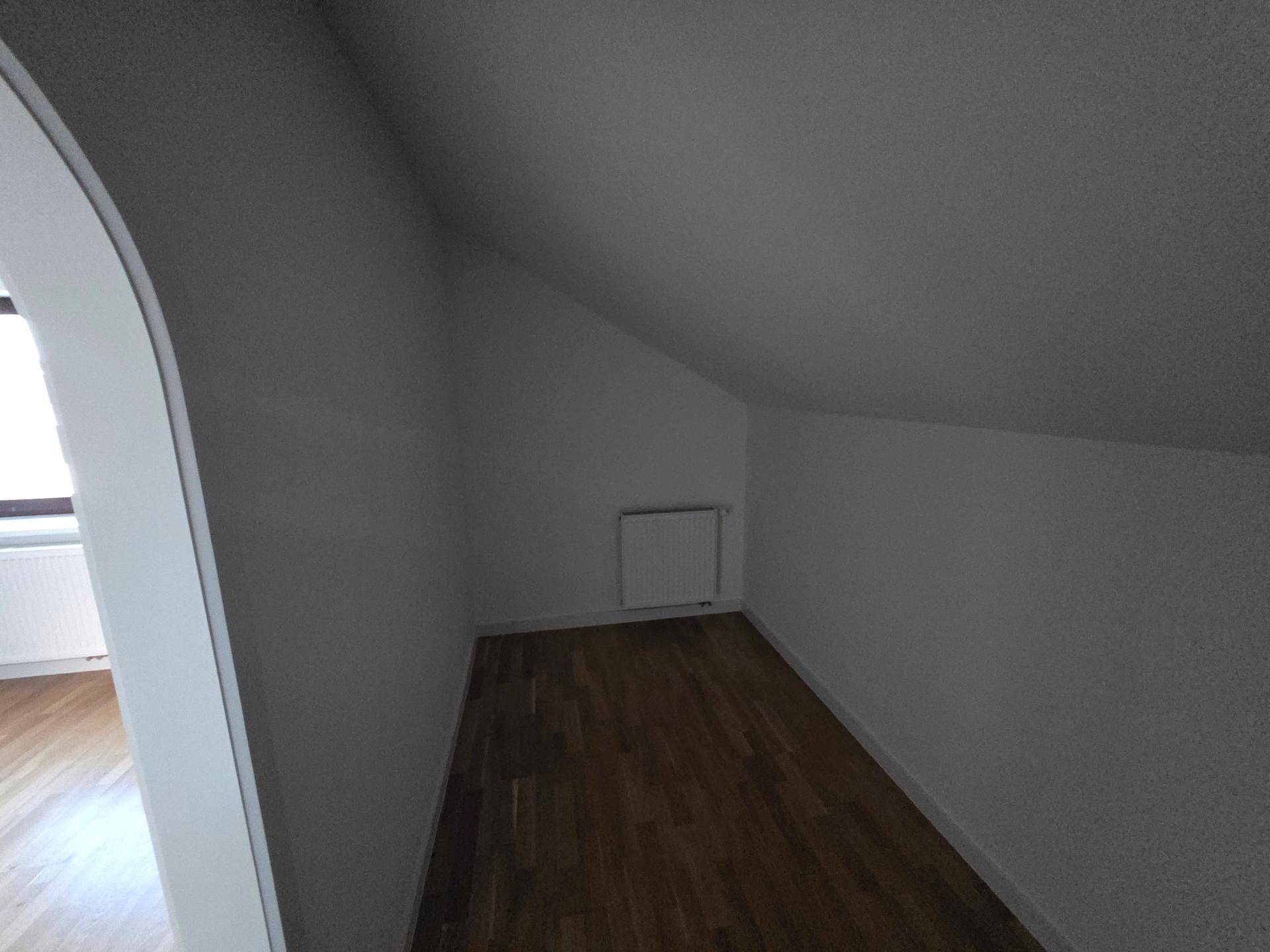 Heller Dachbodenraum mit schrägen Wänden, Holzboden und Heizkörper, ideal als Abstellraum.