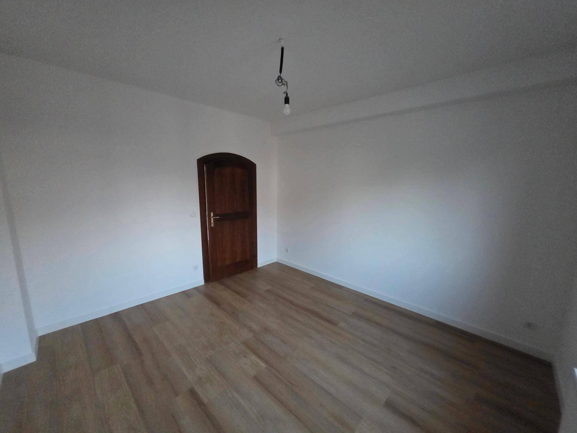 Geräumiges Schlafzimmer mit Laminatboden, weißen Wänden und einer Holztür.