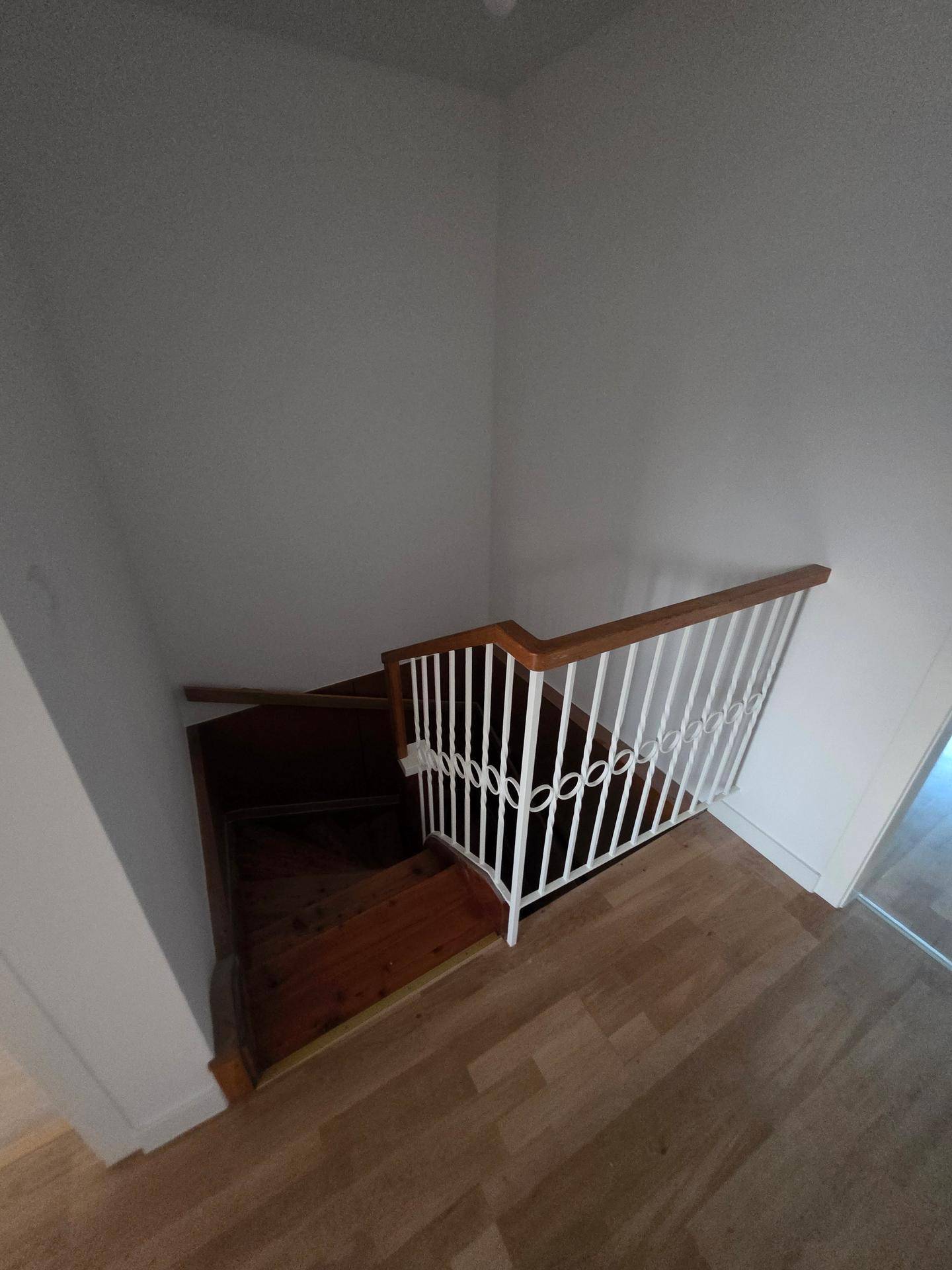 Holztreppe mit weißem Geländer, die in ein Untergeschoss führt.