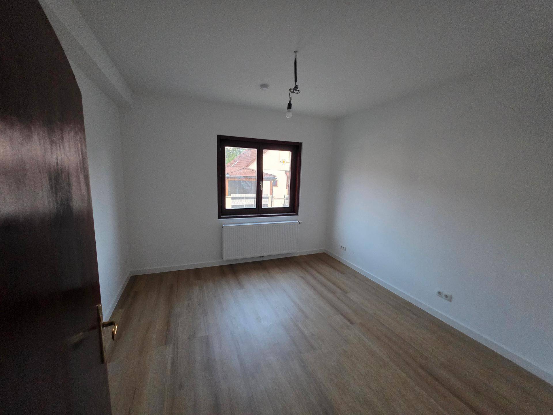 Helles Schlafzimmer mit Laminatboden, Heizkörper und Fenster mit Blick ins Grüne.