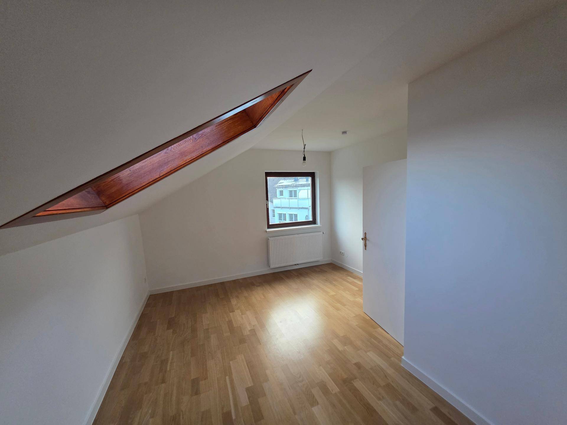 Helles Schlafzimmer im Dachgeschoss mit Holzboden, Fenster und zusätzlichem Dachfenster.