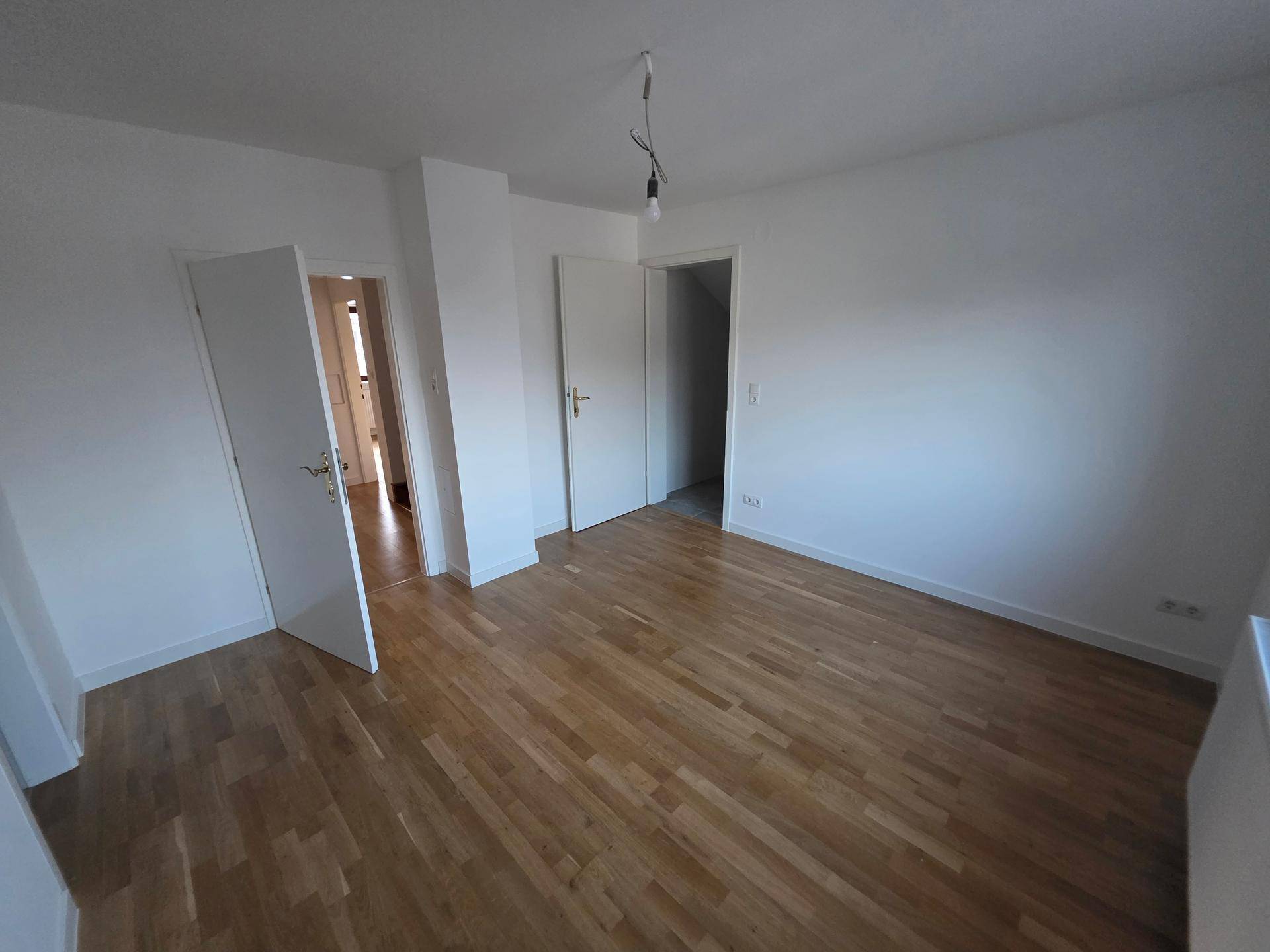 Heller Wohnraum mit Holzfußboden und mehreren Türen, bietet flexible Gestaltungsmöglichkeiten.