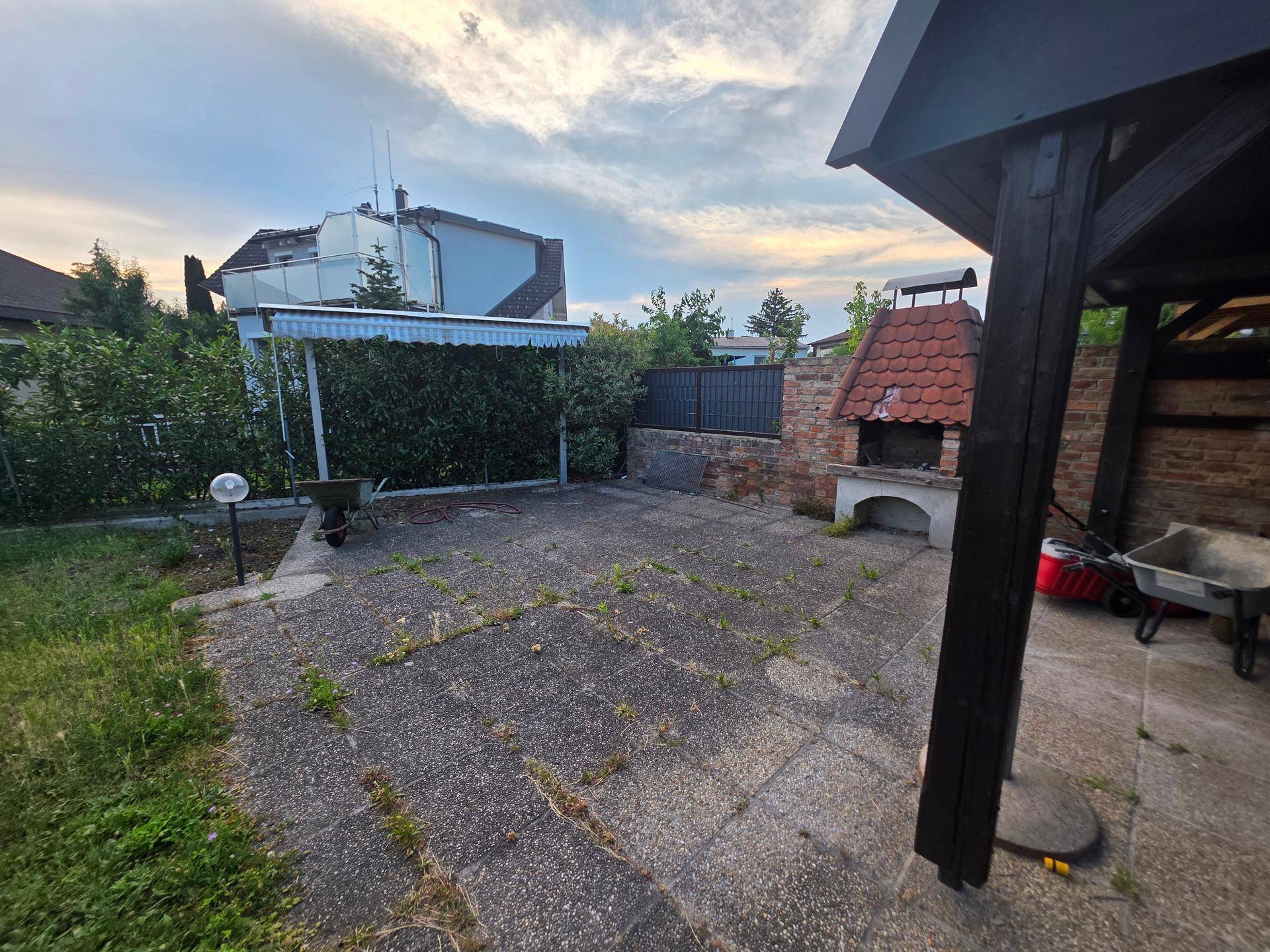 Gepflasterte Terrasse mit gemauertem Grill und überdachtem Bereich im Garten.
