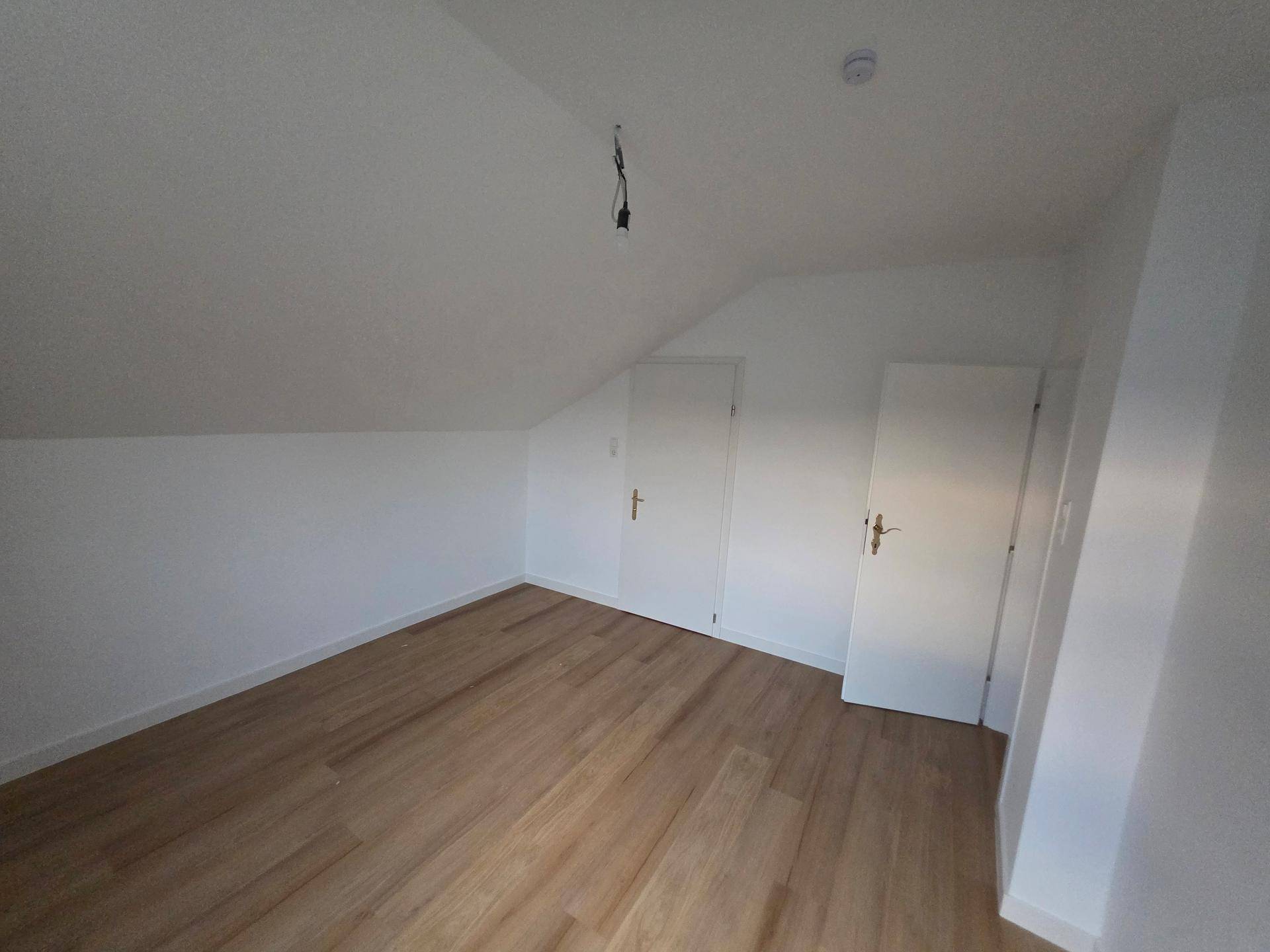 Helles Schlafzimmer im Dachgeschoss mit Holzboden und integrierten Einbauschränken.