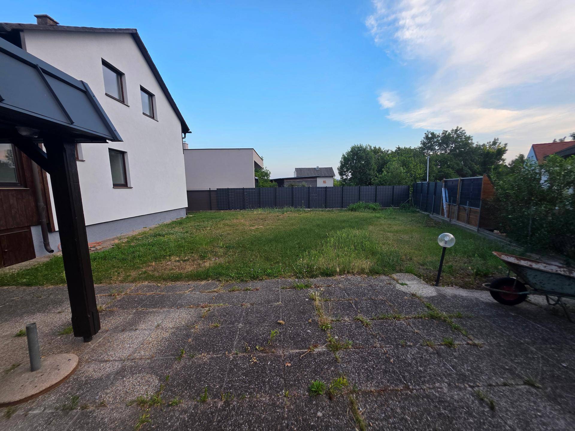 Großer Gartenbereich hinter dem Haus mit Rasenfläche und einer gepflasterten Terrasse.
