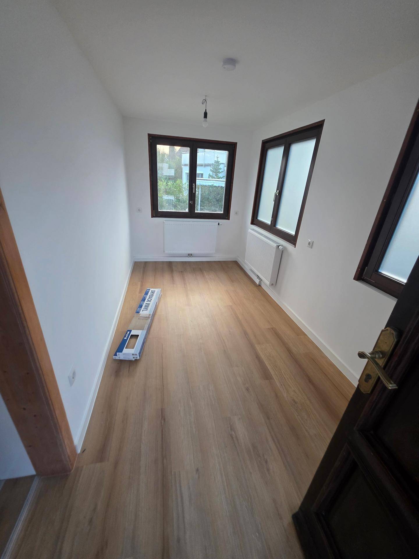 Heller Raum mit neuem Laminatboden, weißen Wänden und mehreren Fenstern.