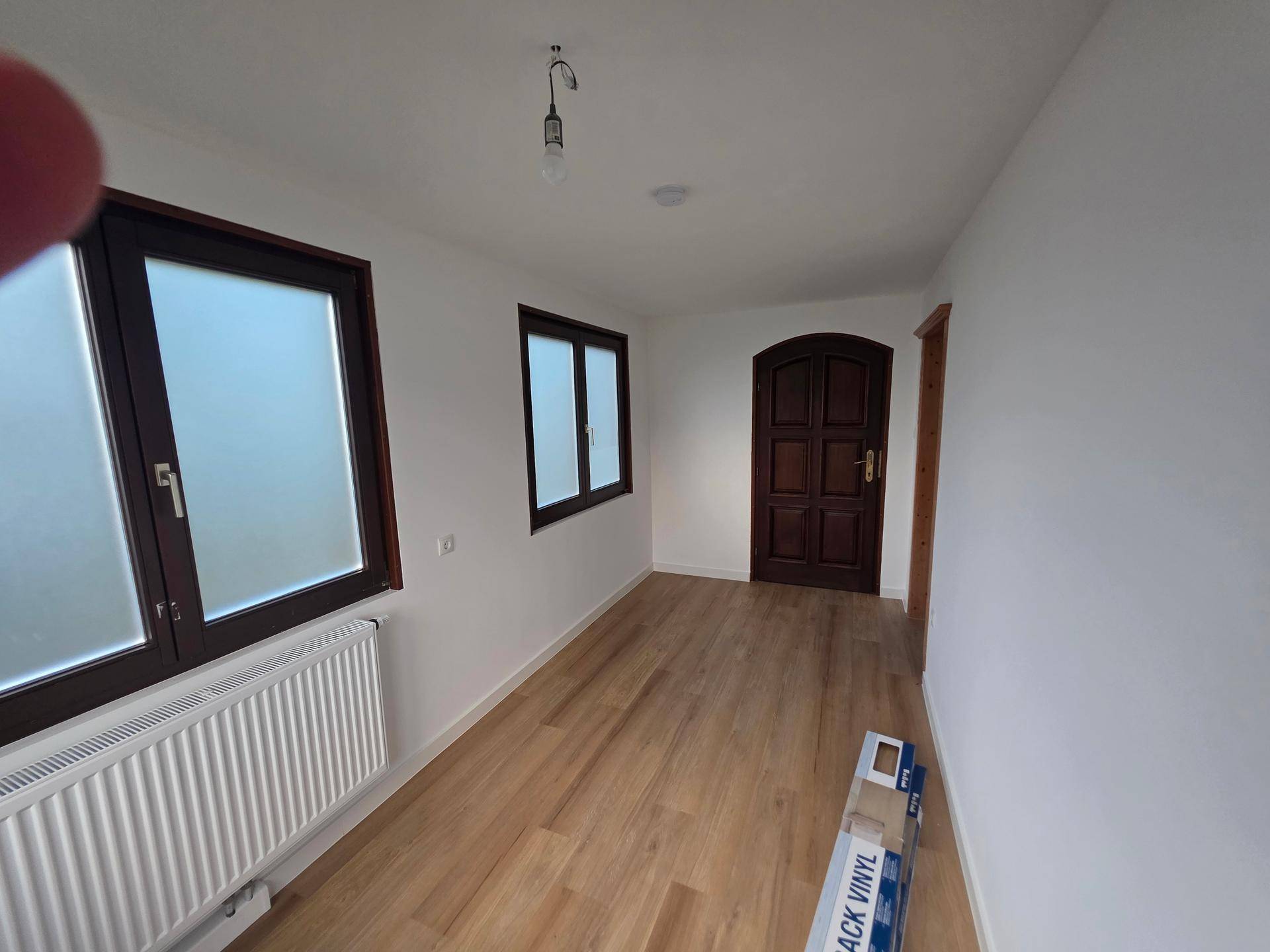 Langer, heller Flur mit Laminatboden, weißen Wänden und einer Holztür.