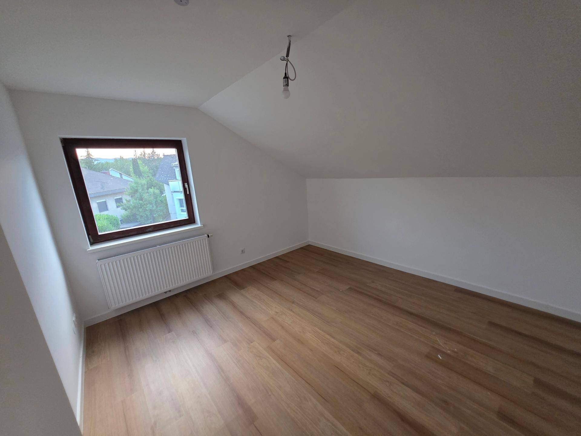 Helles Schlafzimmer im Dachgeschoss mit Holzboden und Fenster, bietet einen Ausblick ins Grüne.