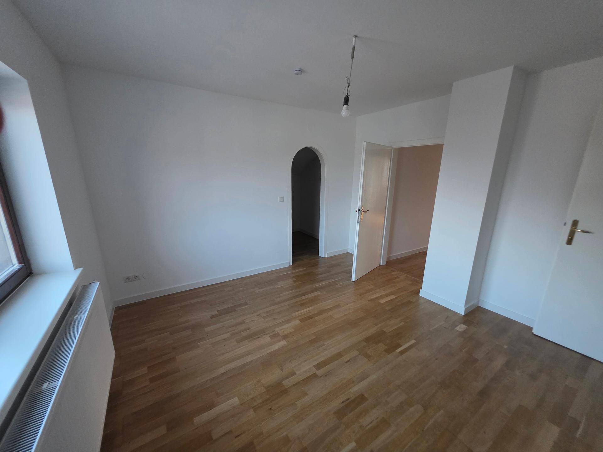 Geräumiger, heller Raum mit Holzfußboden und großem Fenster, vielseitig nutzbar.