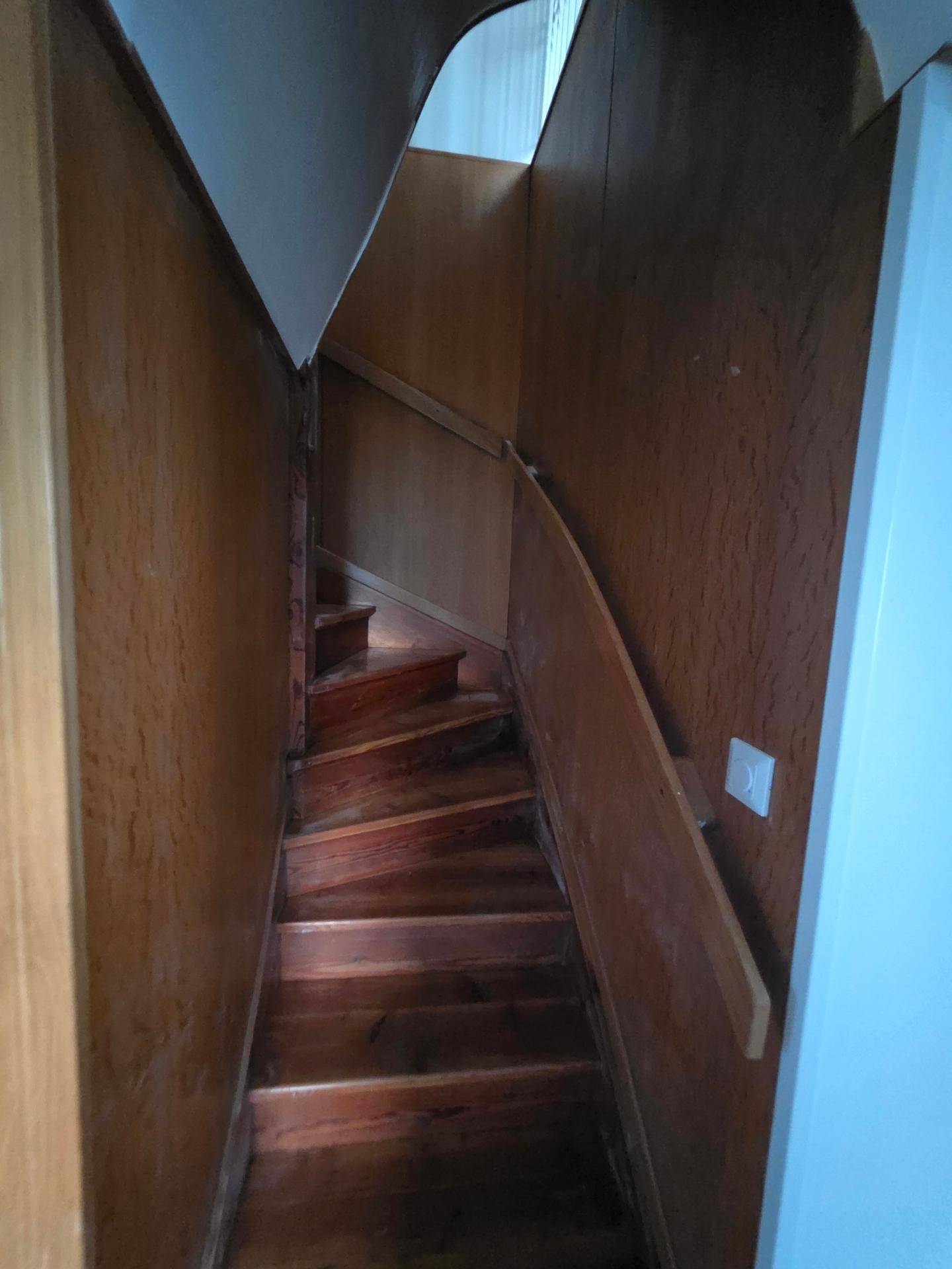 Holztreppe mit dunklen Stufen und Holzverkleidung, die in ein Obergeschoss führt.