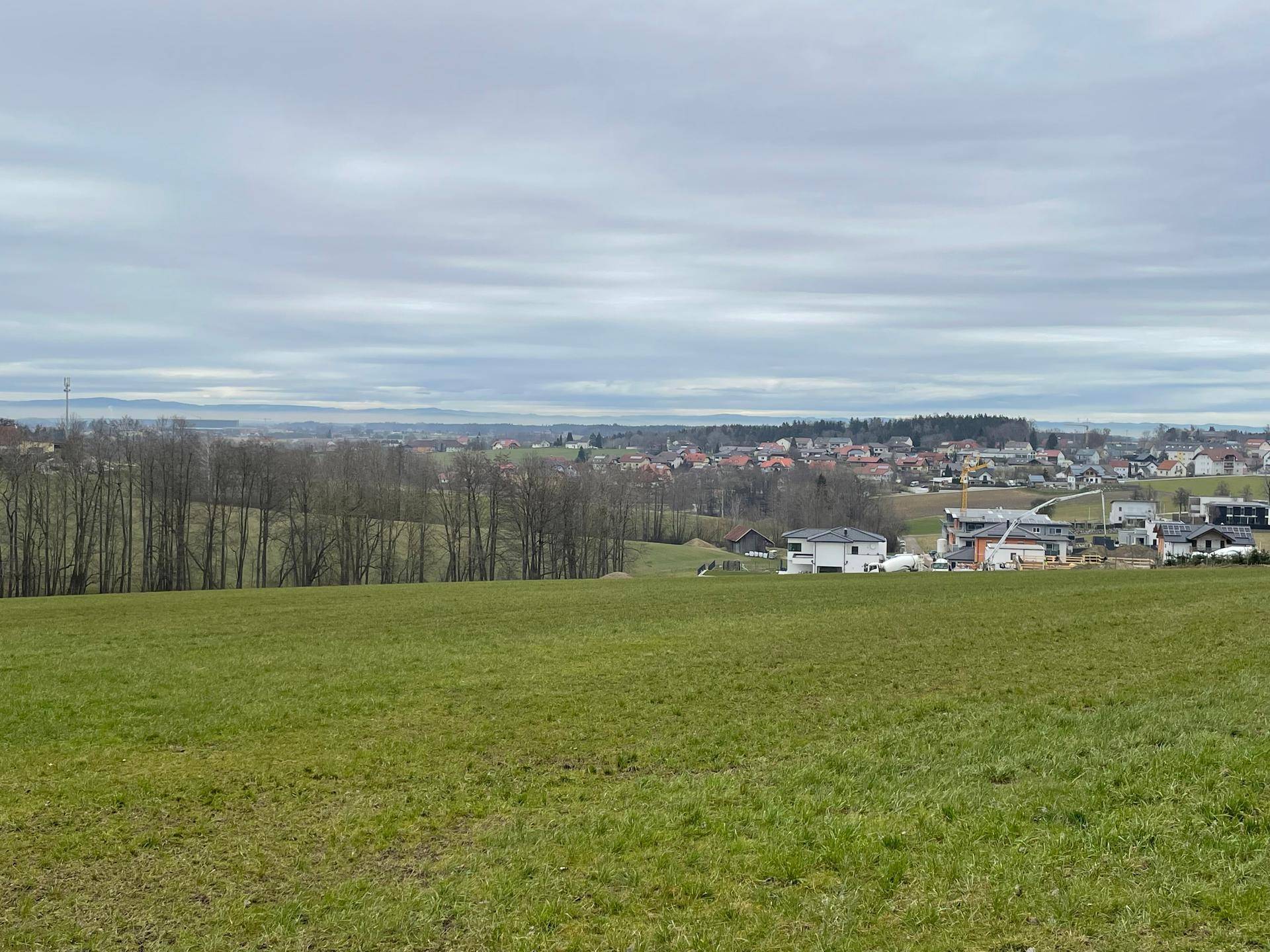 Ausblick auf eine weite grüne Landschaft mit einem Dorf in der Ferne und einem bewölkten Himmel.