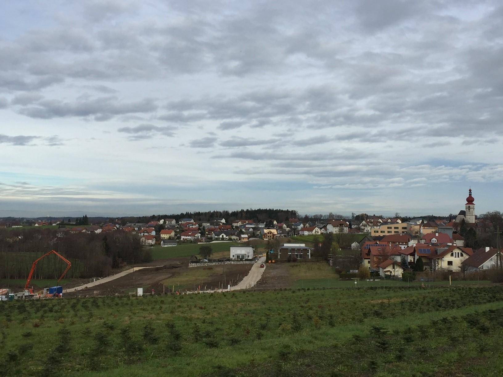 Blick über eine ländliche Gegend mit einem Dorf, Baustellen und einem Kirchturm unter grauem Himmel.