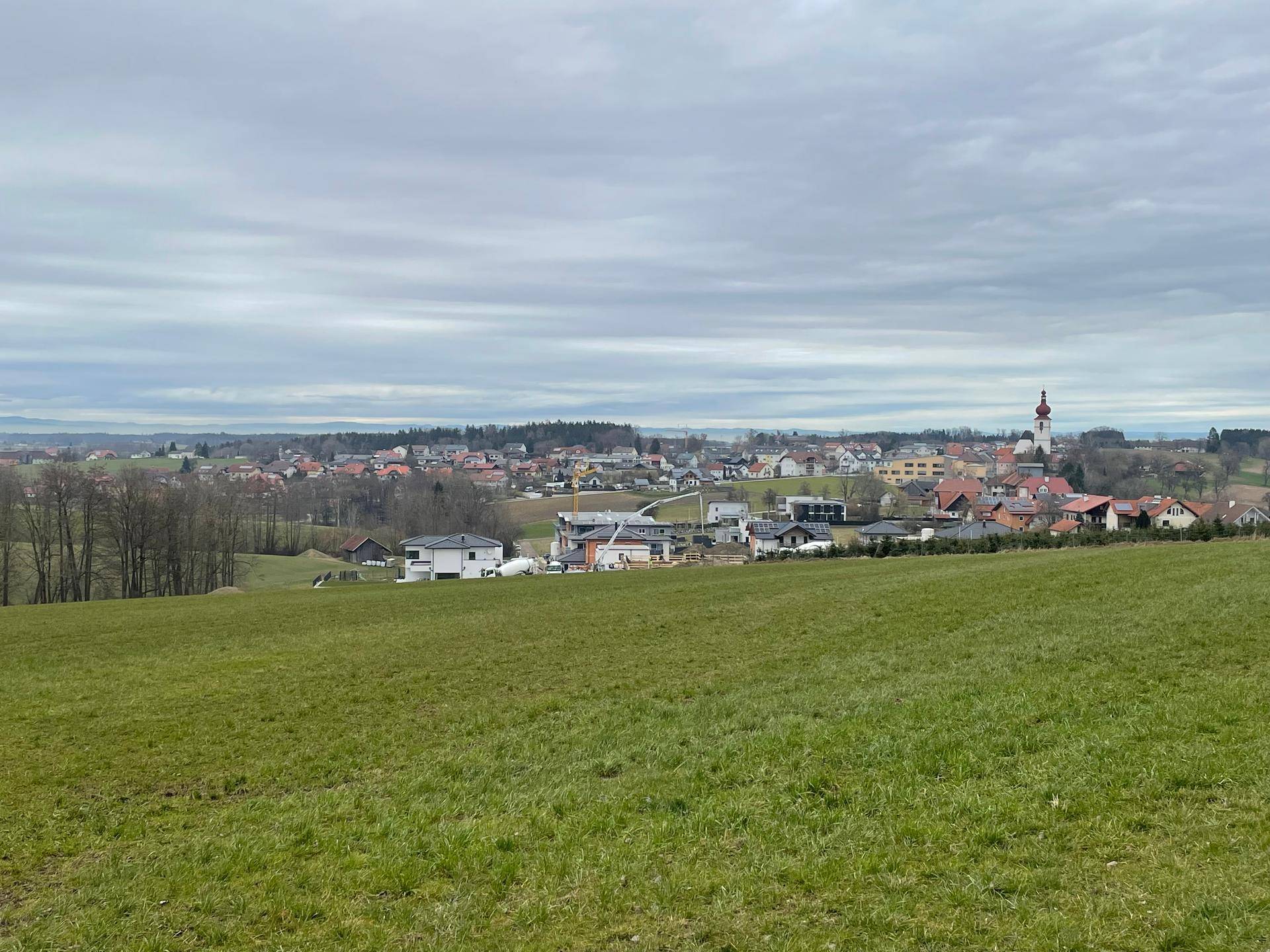 Panoramablick über sanfte Hügel und ein ländliches Dorf mit verstreuten Häusern und einem Kirchturm.
