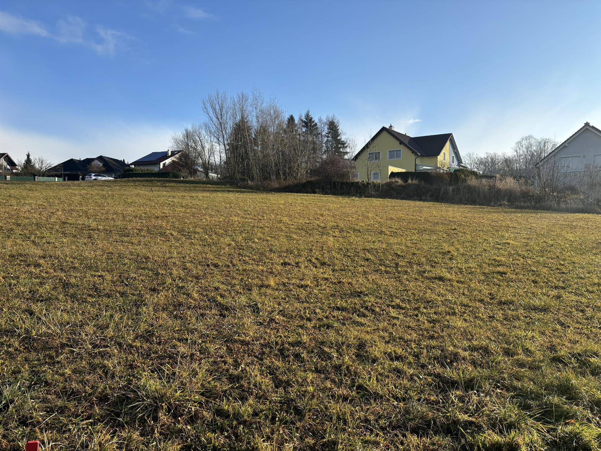 Großes, offenes Grundstück mit Grasfläche und vereinzelten Wohnhäusern am Horizont unter strahlendem Himmel.