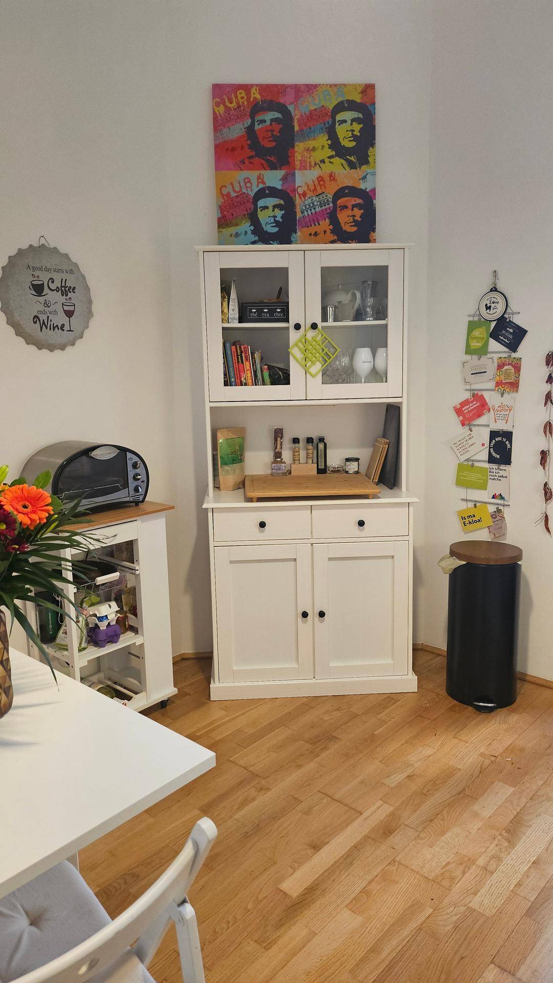 Essbereich mit weißem Vitrinenschrank, farbenfroher Kunst und Holzboden.