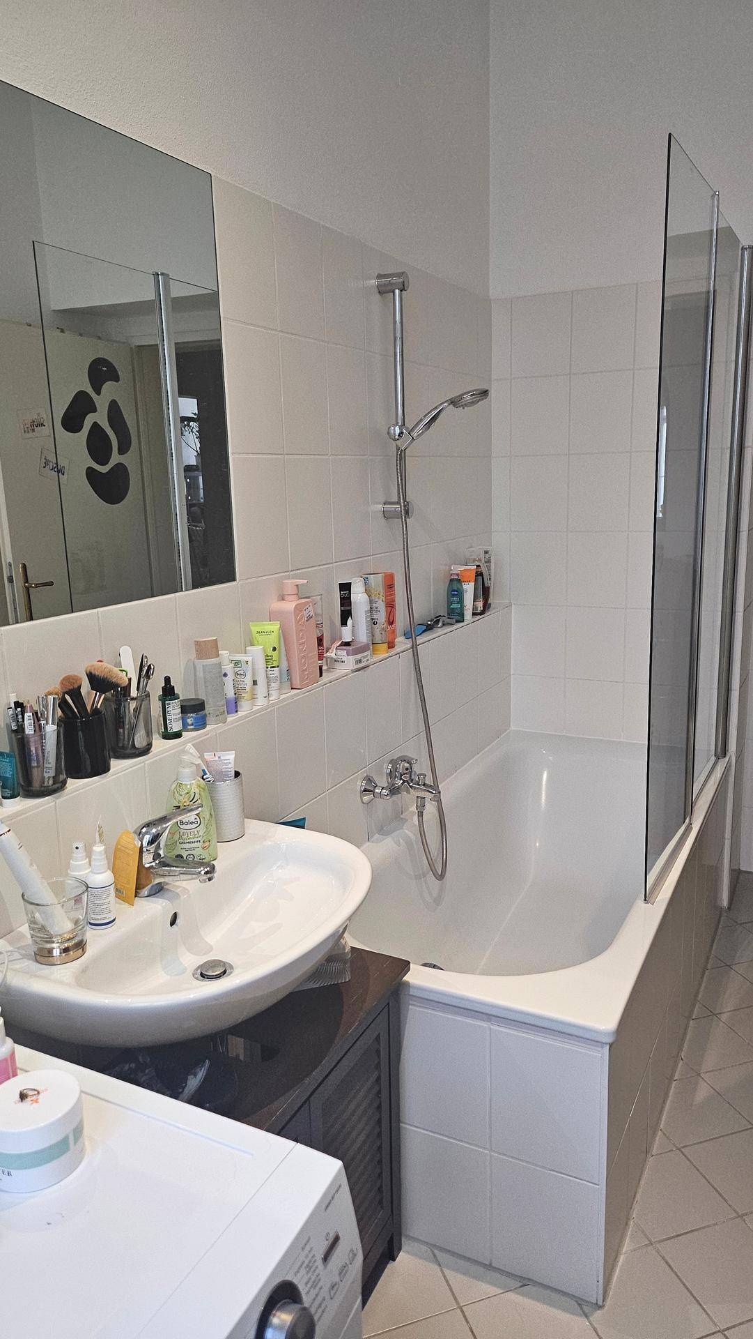 Badezimmer mit Waschbecken, Badewanne mit Duschvorrichtung und großem Spiegel.