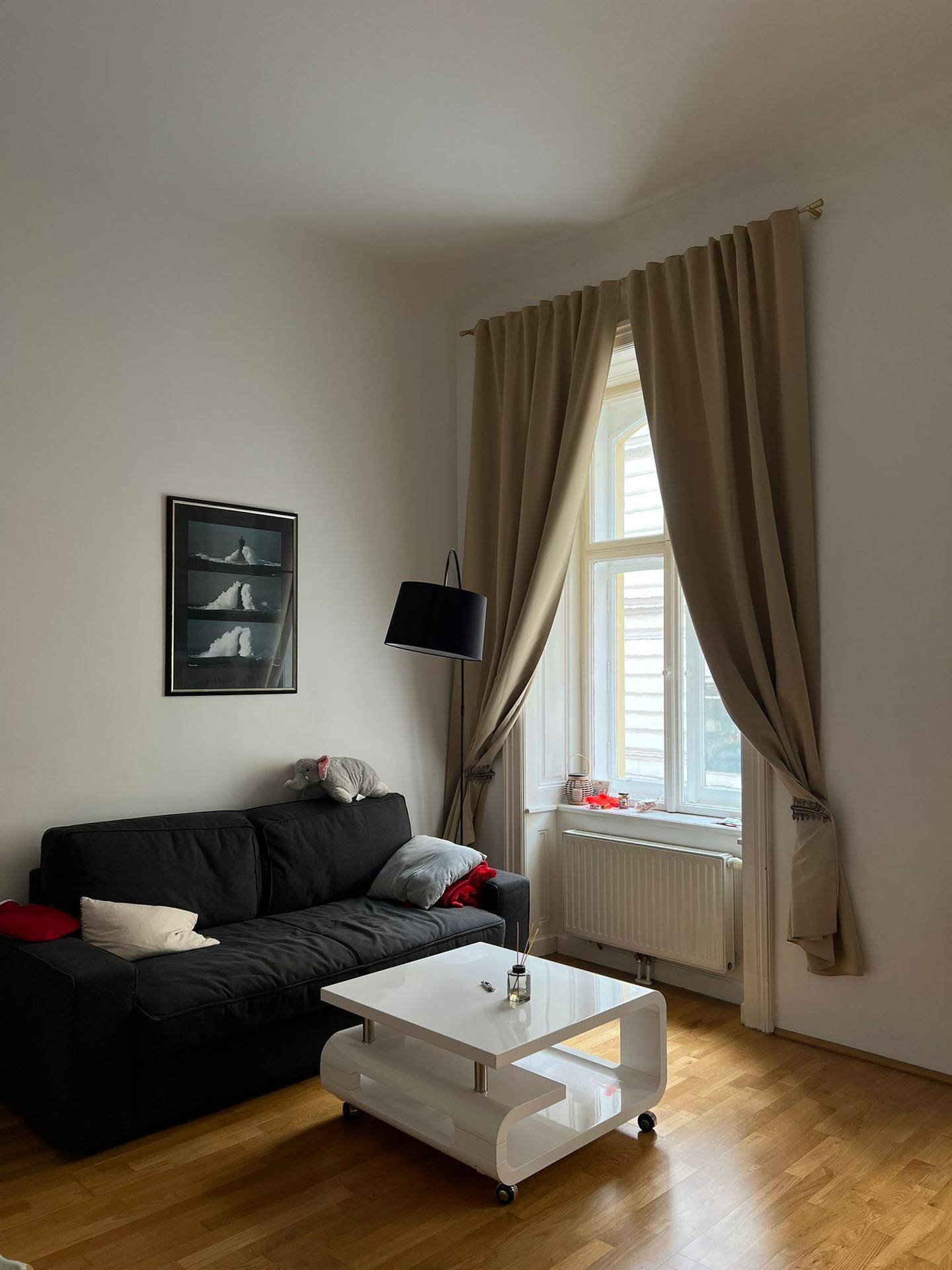 Gemütlicher Wohnbereich mit dunklem Sofa, weißem Couchtisch und hellem Parkettboden.