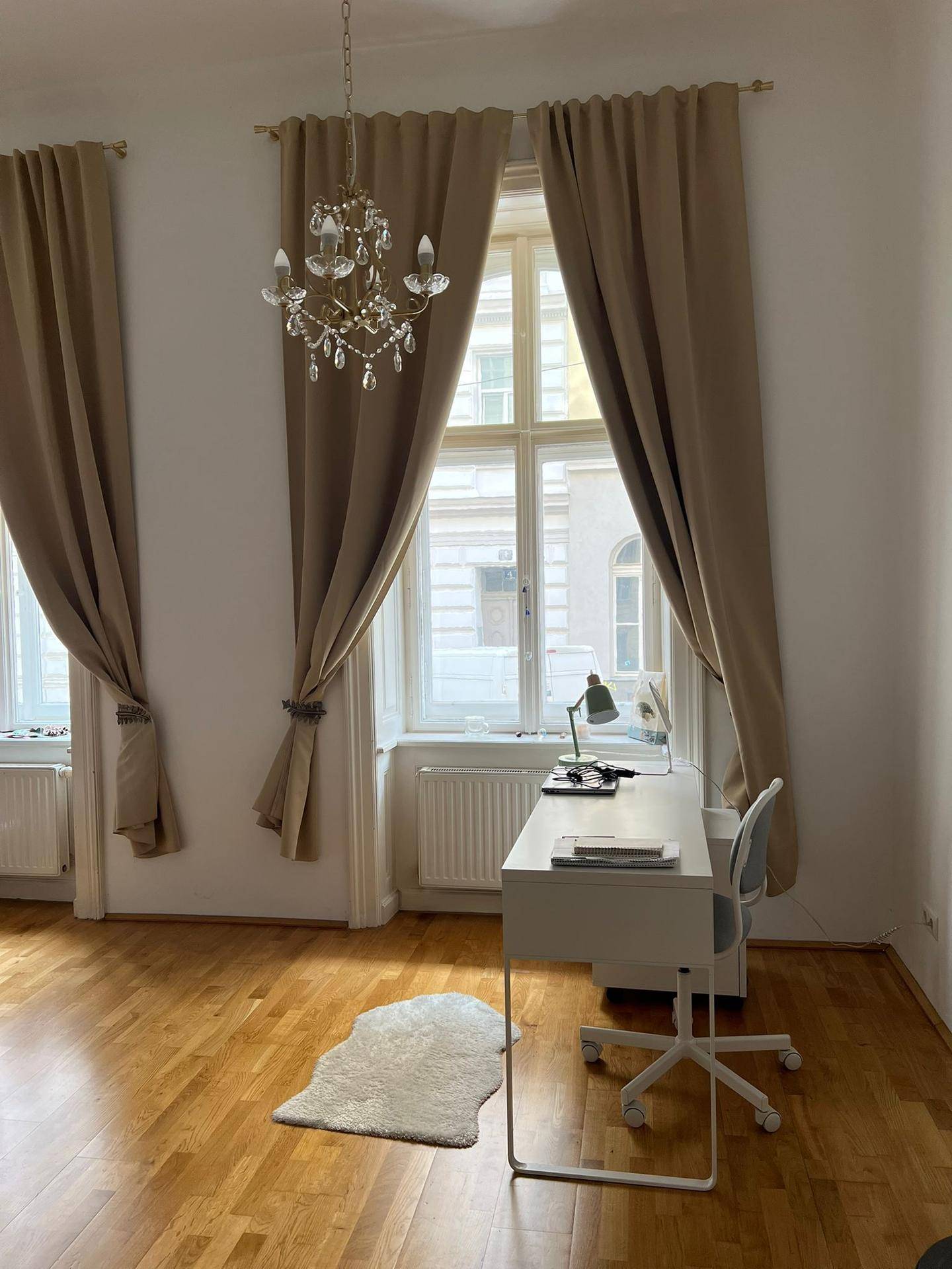 Heller Arbeitsbereich am Fenster mit Schreibtisch, Bürostuhl und Kronleuchter in einem Wohnzimmer.