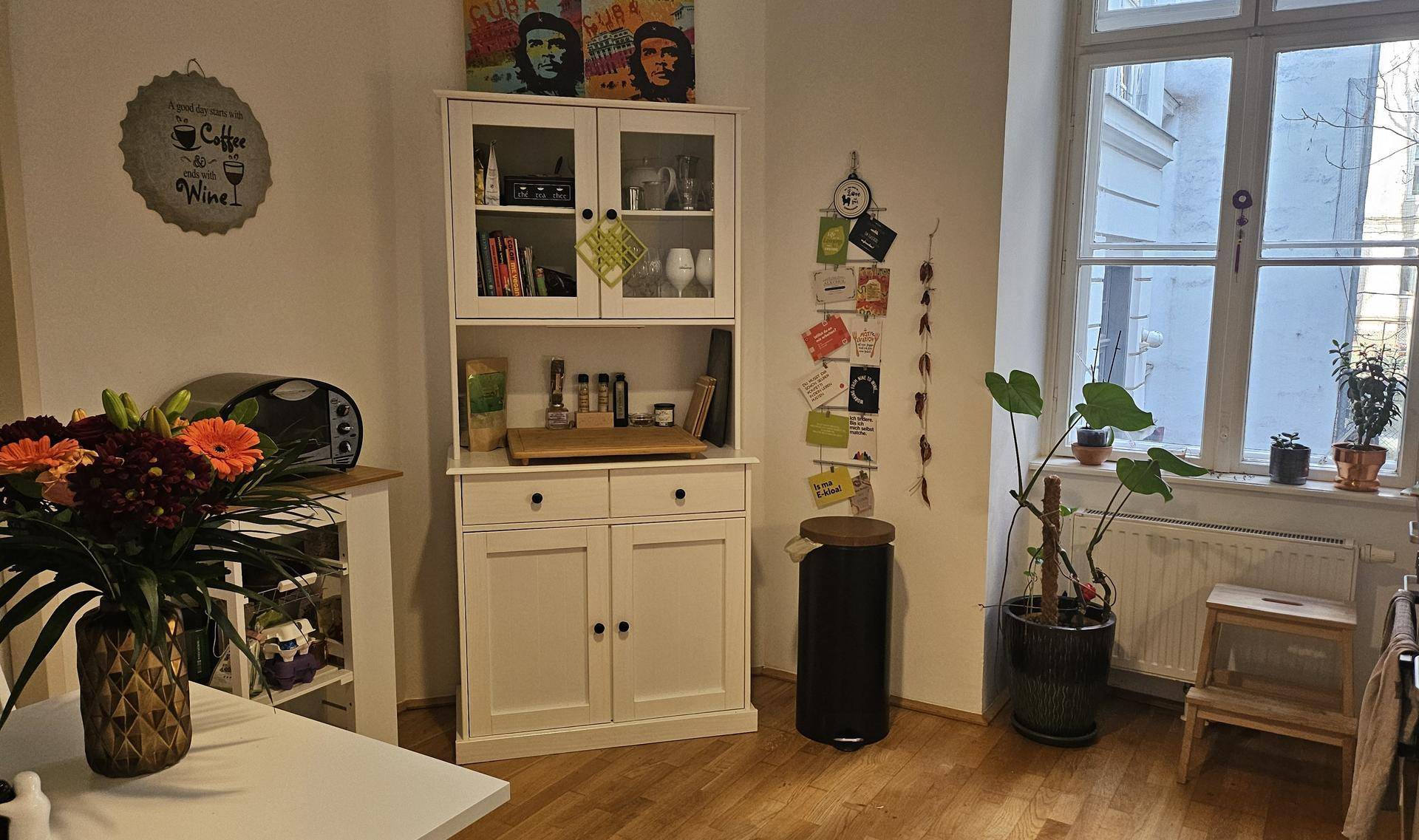 Essbereich in der Küche mit weißem Schrank, Pflanzen und einem Fenster.