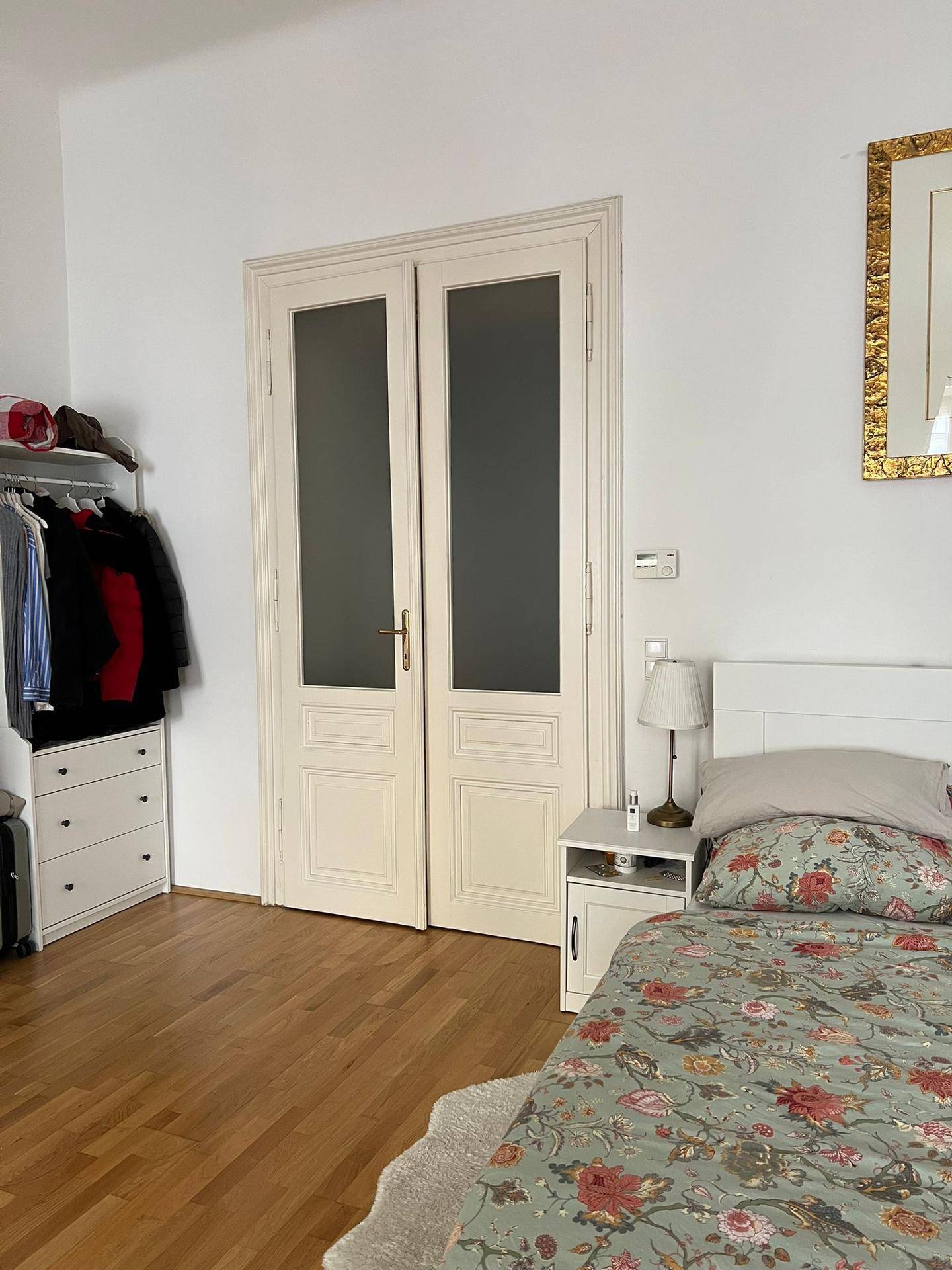 Schlafzimmer mit Holzboden, Nachttisch und Doppeltüren mit Glaseinsätzen.
