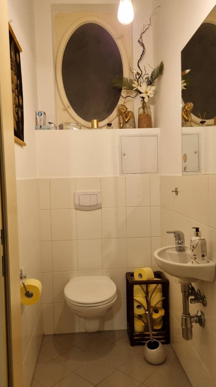 Kleines Gäste-WC mit Toilette, Waschbecken und ovalem Fenster.