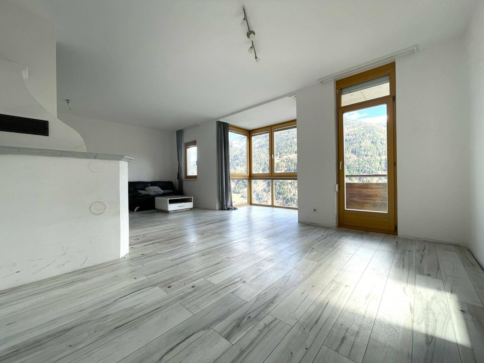 Lichtdurchflutetes Wohnzimmer mit Holzboden und Zugang zum Balkon, bietet weite Ausblicke.