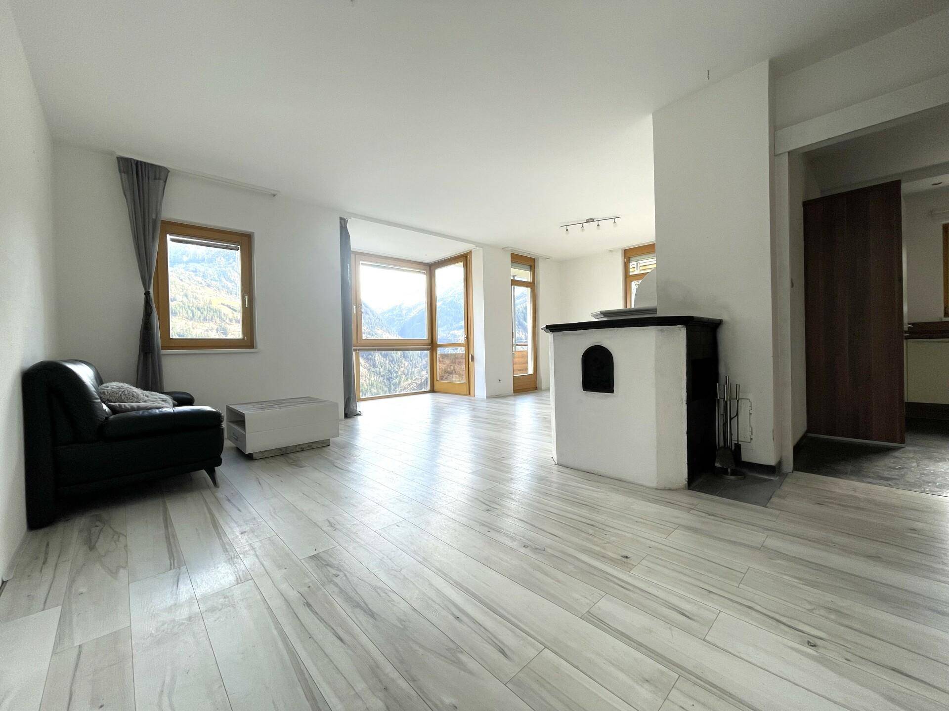 Helles Wohnzimmer mit modernem Holzboden, Kaminofen und großen Fenstern mit Bergblick.