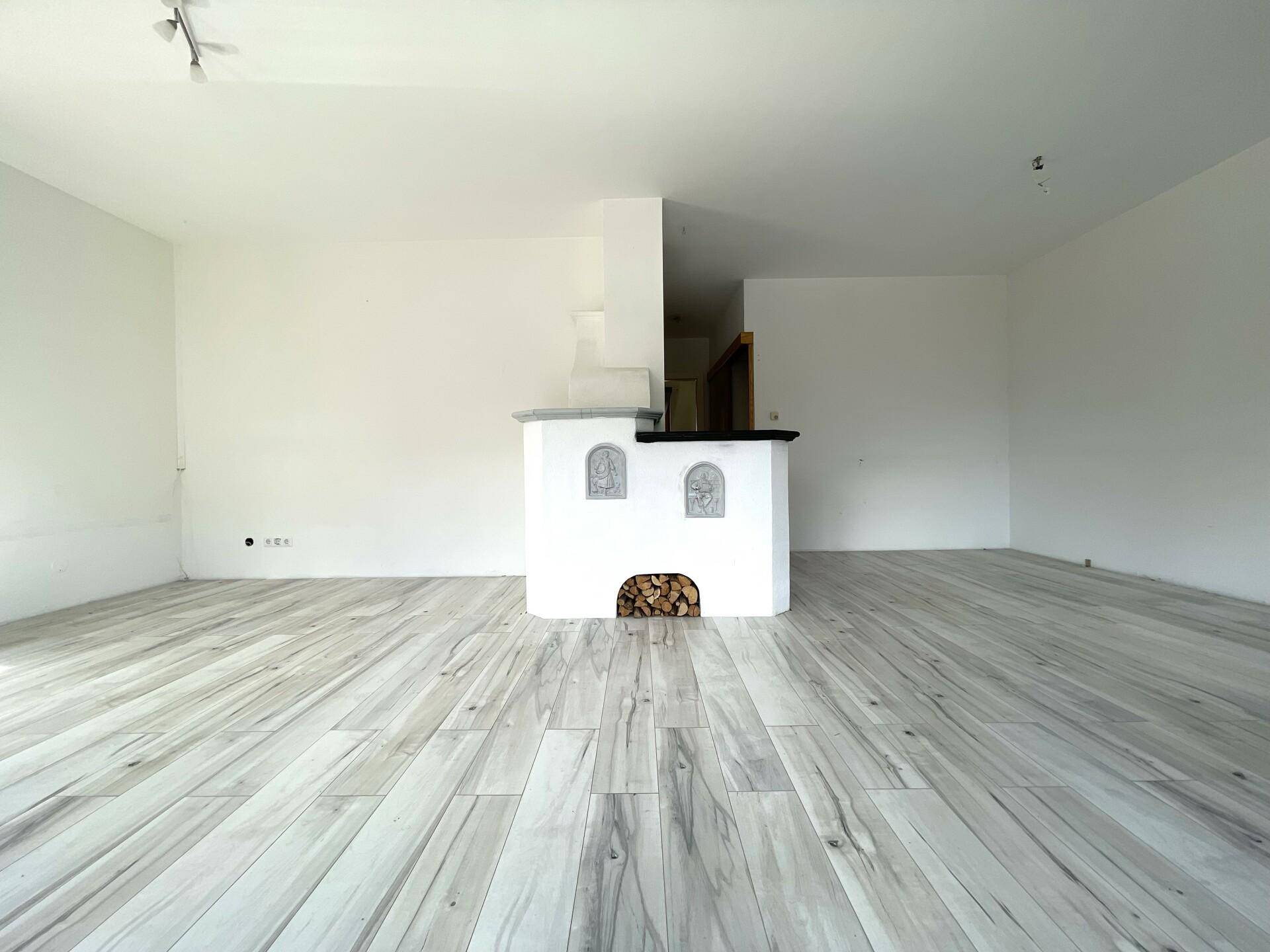 Geräumiges Wohnzimmer mit hellem Holzboden und einem traditionellen Kaminofen als Blickfang.