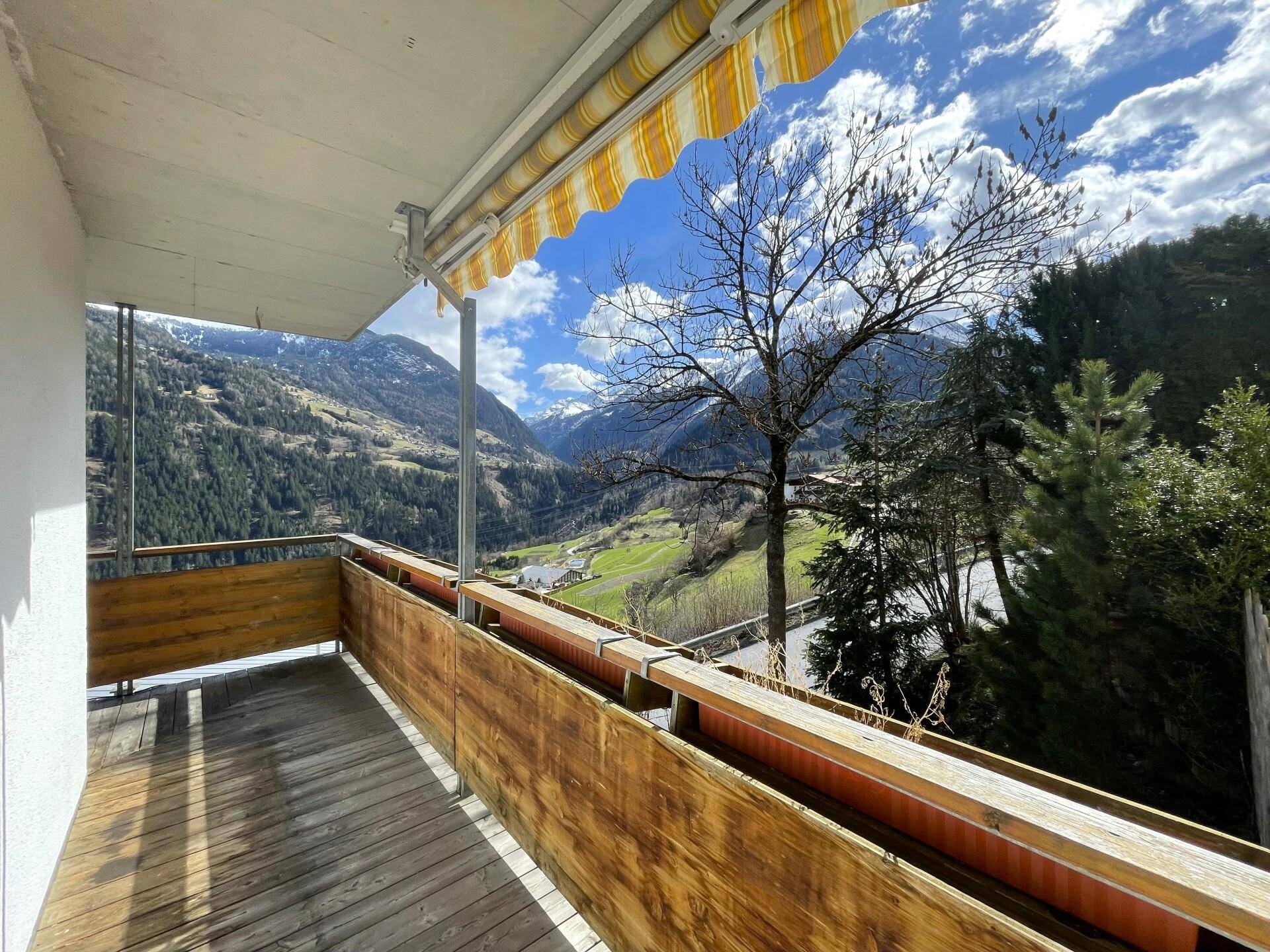 Sonniger Balkon mit Holzgeländer und Markise, ideal zum Entspannen mit Bergblick.