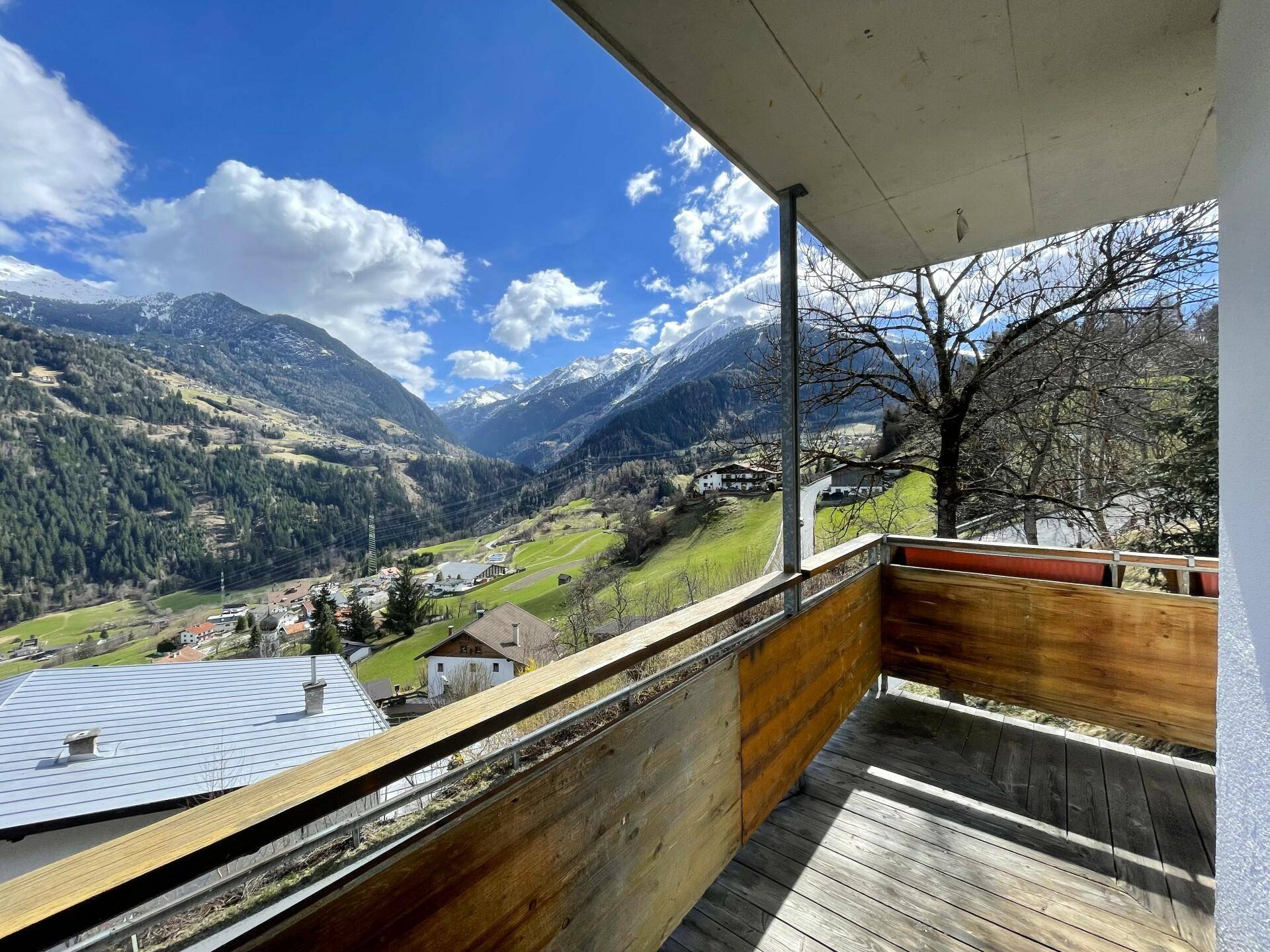Geräumiger Holzbalkon mit atemberaubendem Blick auf die umliegende Berglandschaft und das Tal.