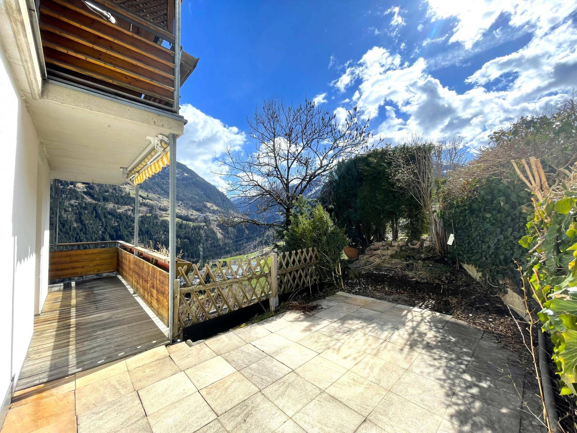 Gepflasterte Terrasse mit Gartenbereich und weitem Blick auf die umliegende Berglandschaft.