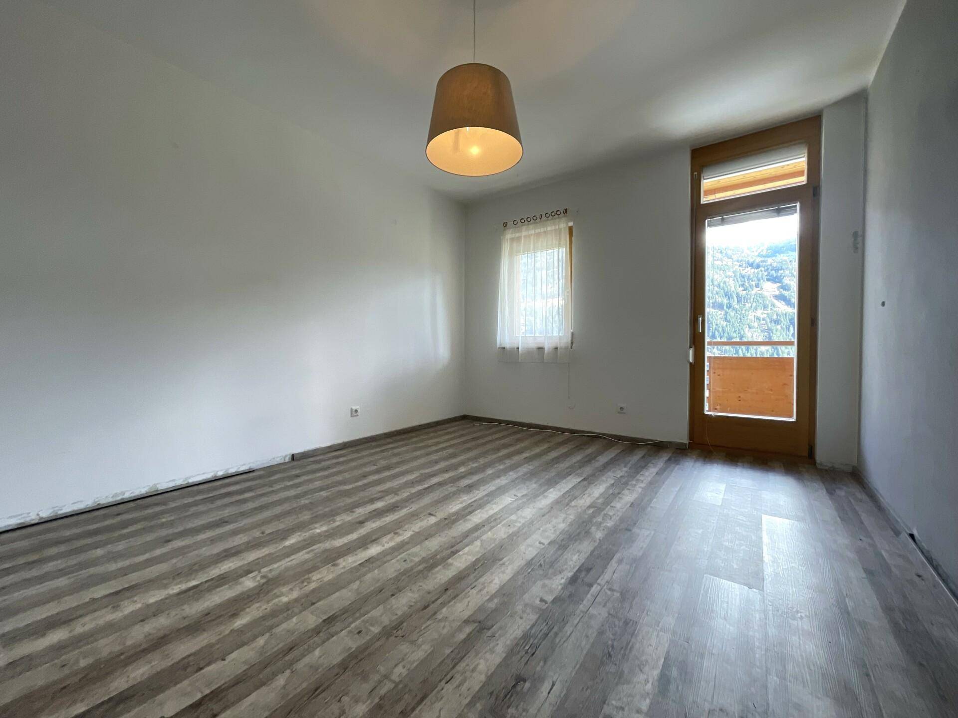 Helles Schlafzimmer mit modernem Laminatboden und Zugang zu einem Balkon mit Bergblick.