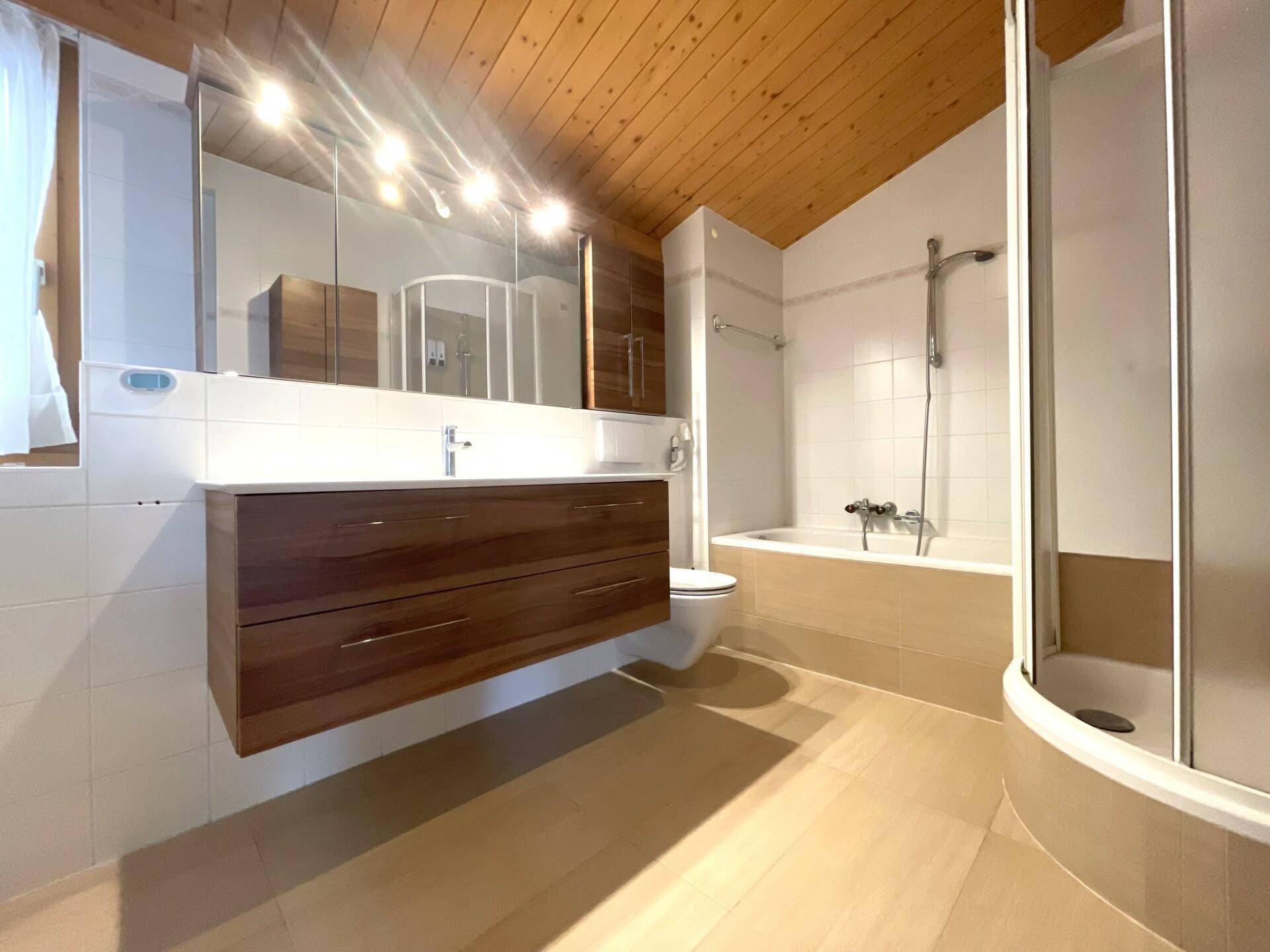Modernes Badezimmer mit Holzwaschtisch, Badewanne und Duschkabine unter einer Holzdecke.