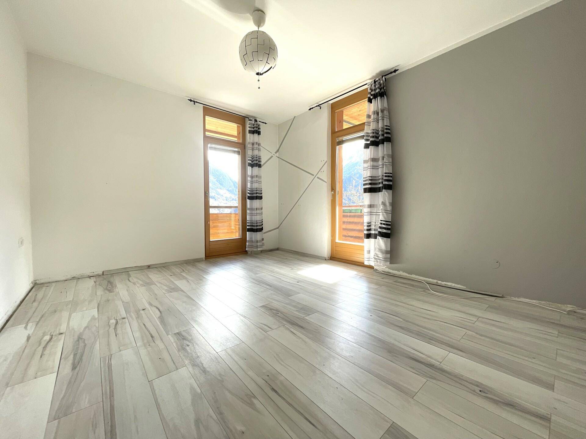 Geräumiges Schlafzimmer mit hellem Holzboden und zwei Fenstertüren, die viel Licht hereinlassen.