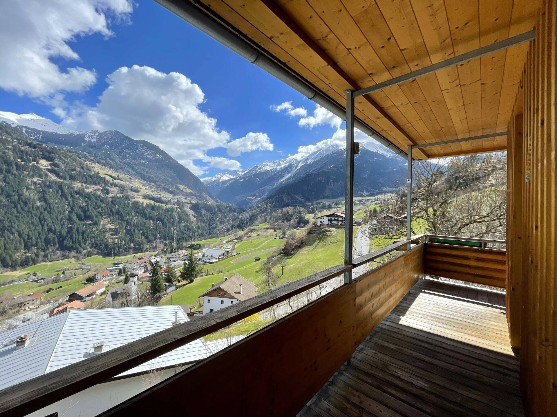 Überdachter Holzbalkon mit weitem Blick auf die grüne Berglandschaft und das Tal.