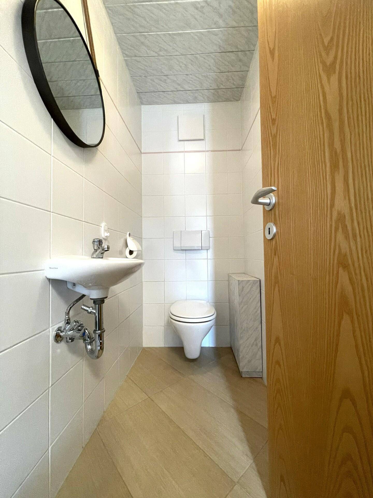 Kleines Gäste-WC mit weißen Fliesen, wandhängendem WC und Handwaschbecken.
