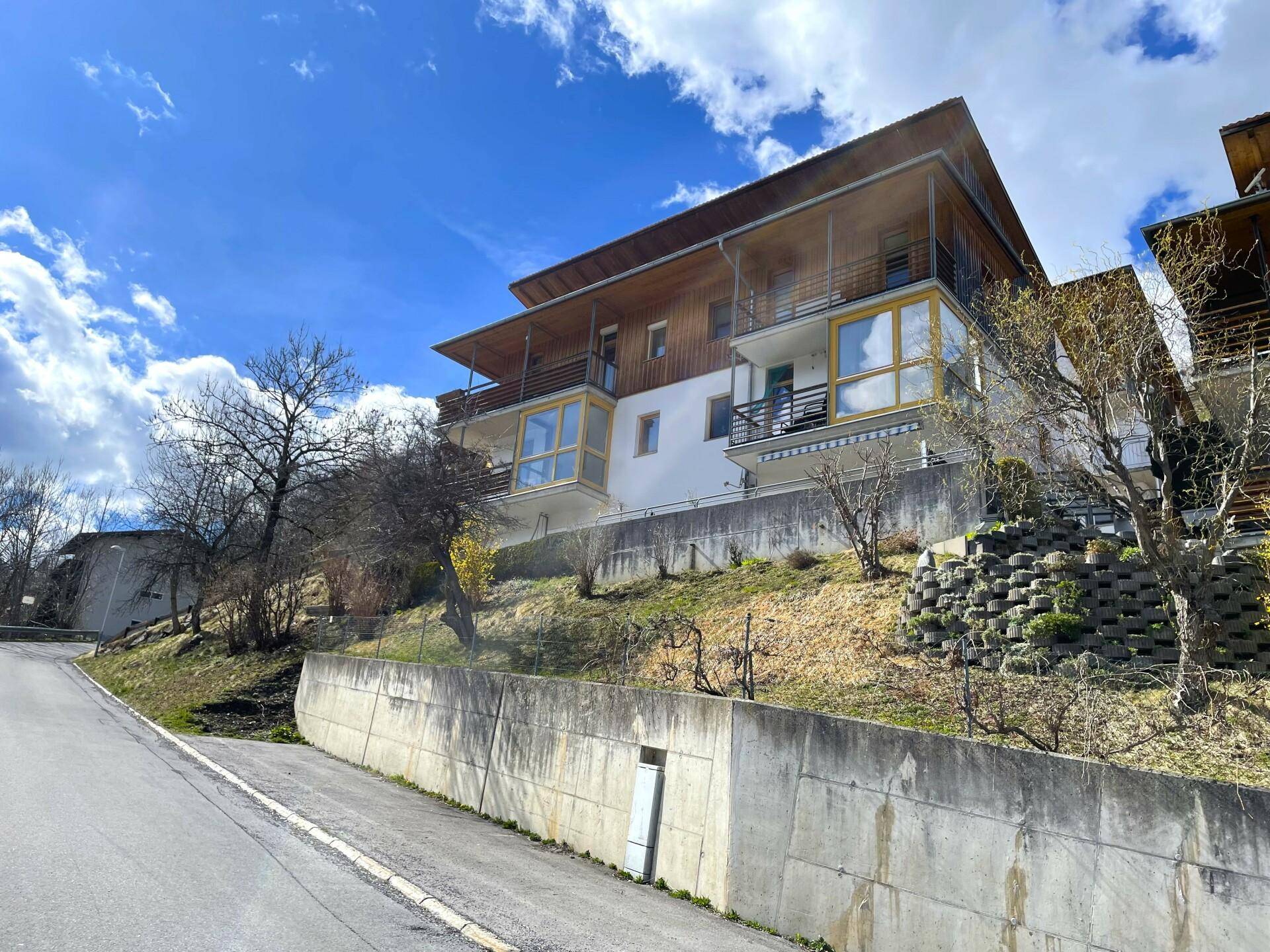 Mehrfamilienhaus in Hanglage mit mehreren Balkonen und Terrassen, umgeben von Natur.