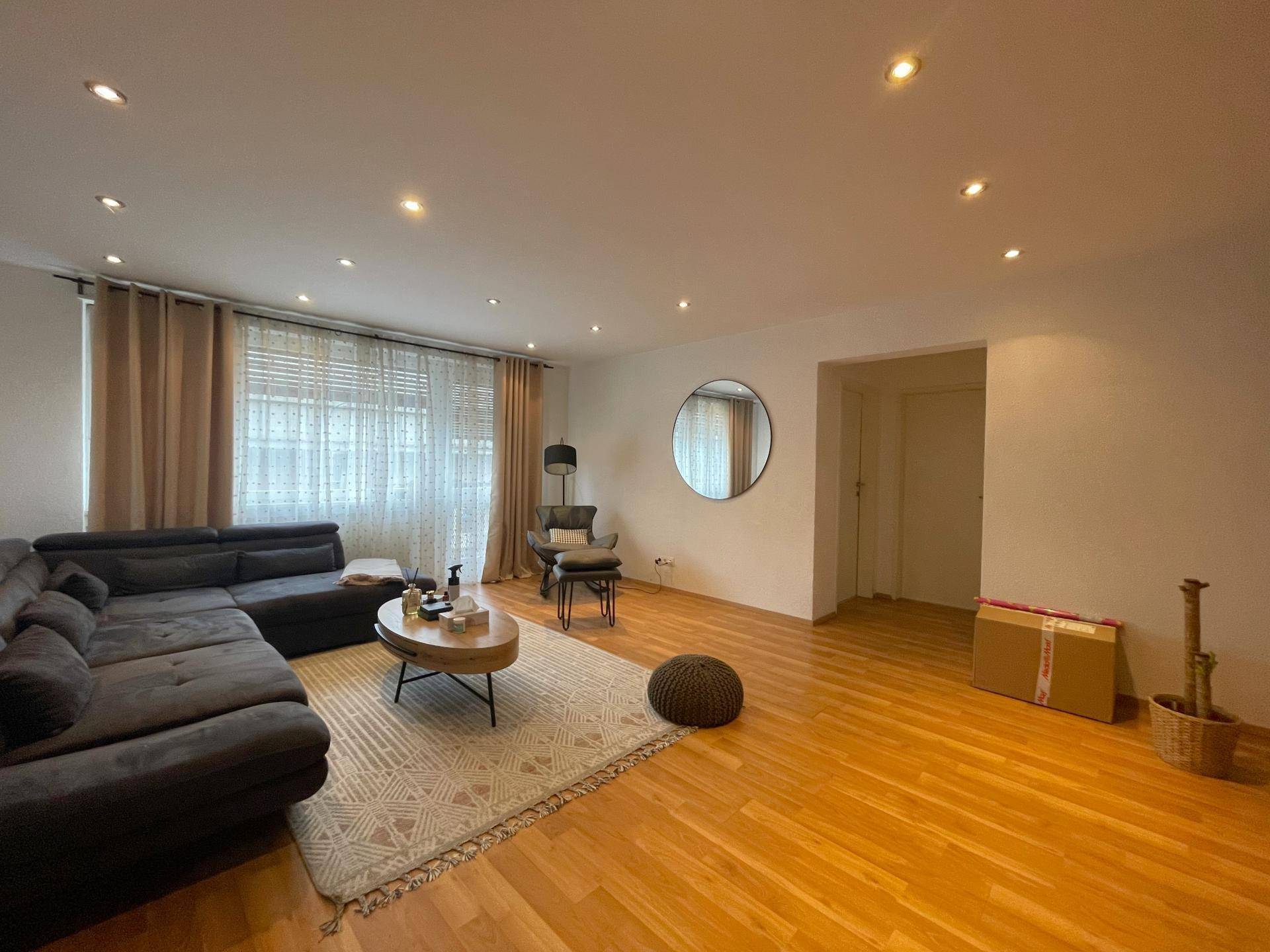 Helles Wohnzimmer mit Parkettboden, großem Ecksofa und indirekter Deckenbeleuchtung.