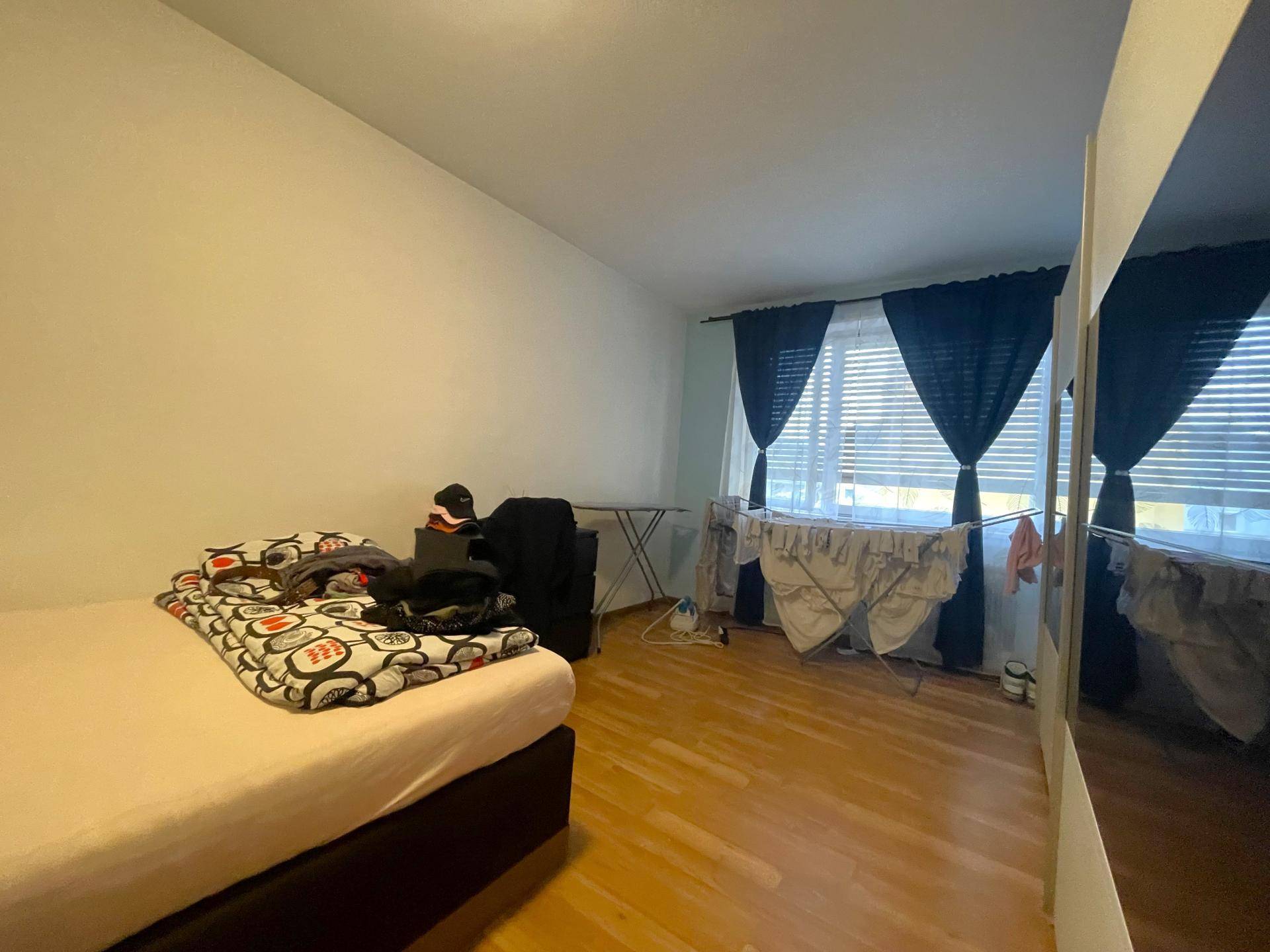 Schlichtes Schlafzimmer mit Holzboden, Fenster und einem großen Spiegel an der Wand.