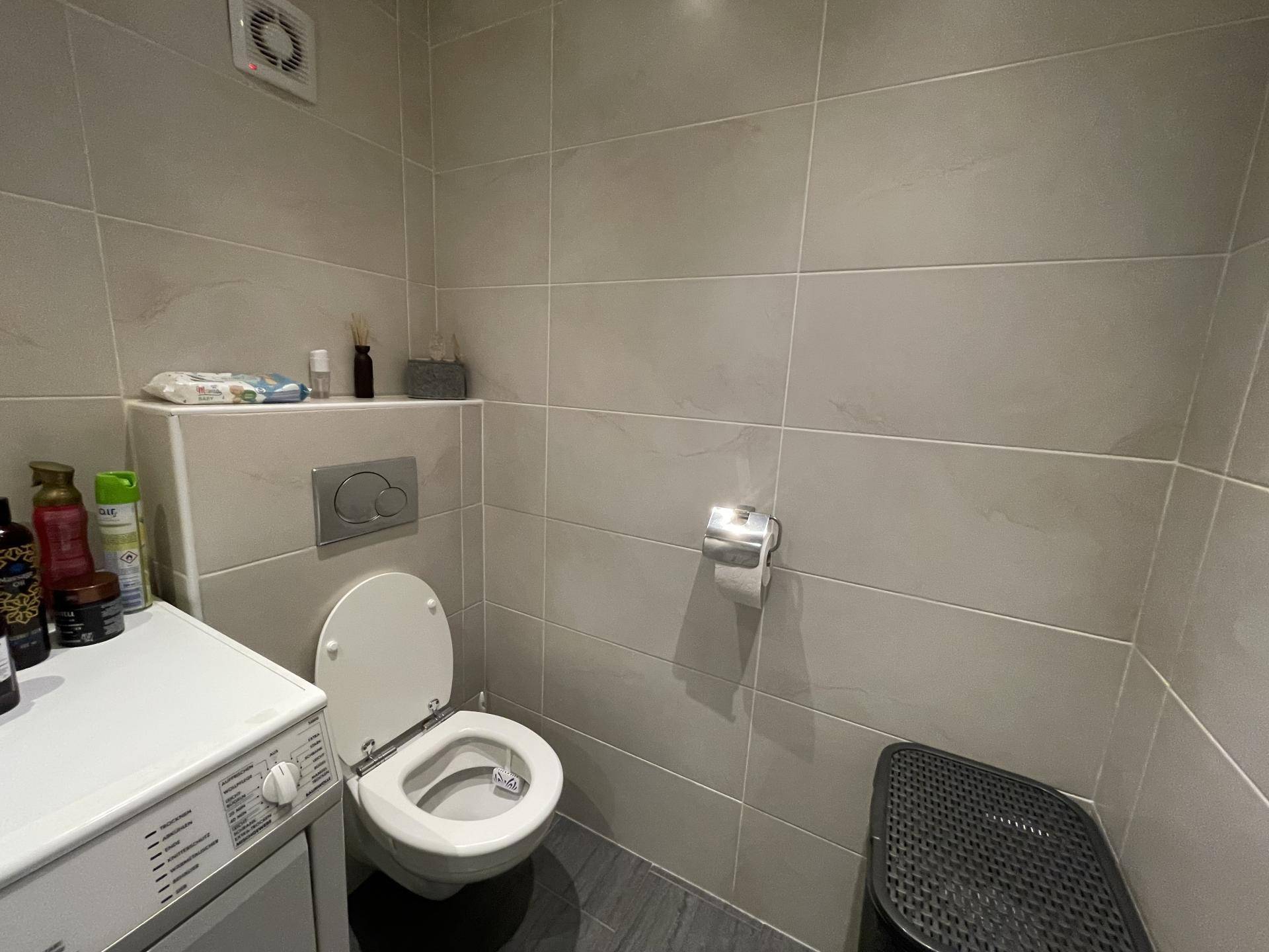 Separates WC mit Wand-WC, Fliesen an den Wänden und einer Waschmaschine.