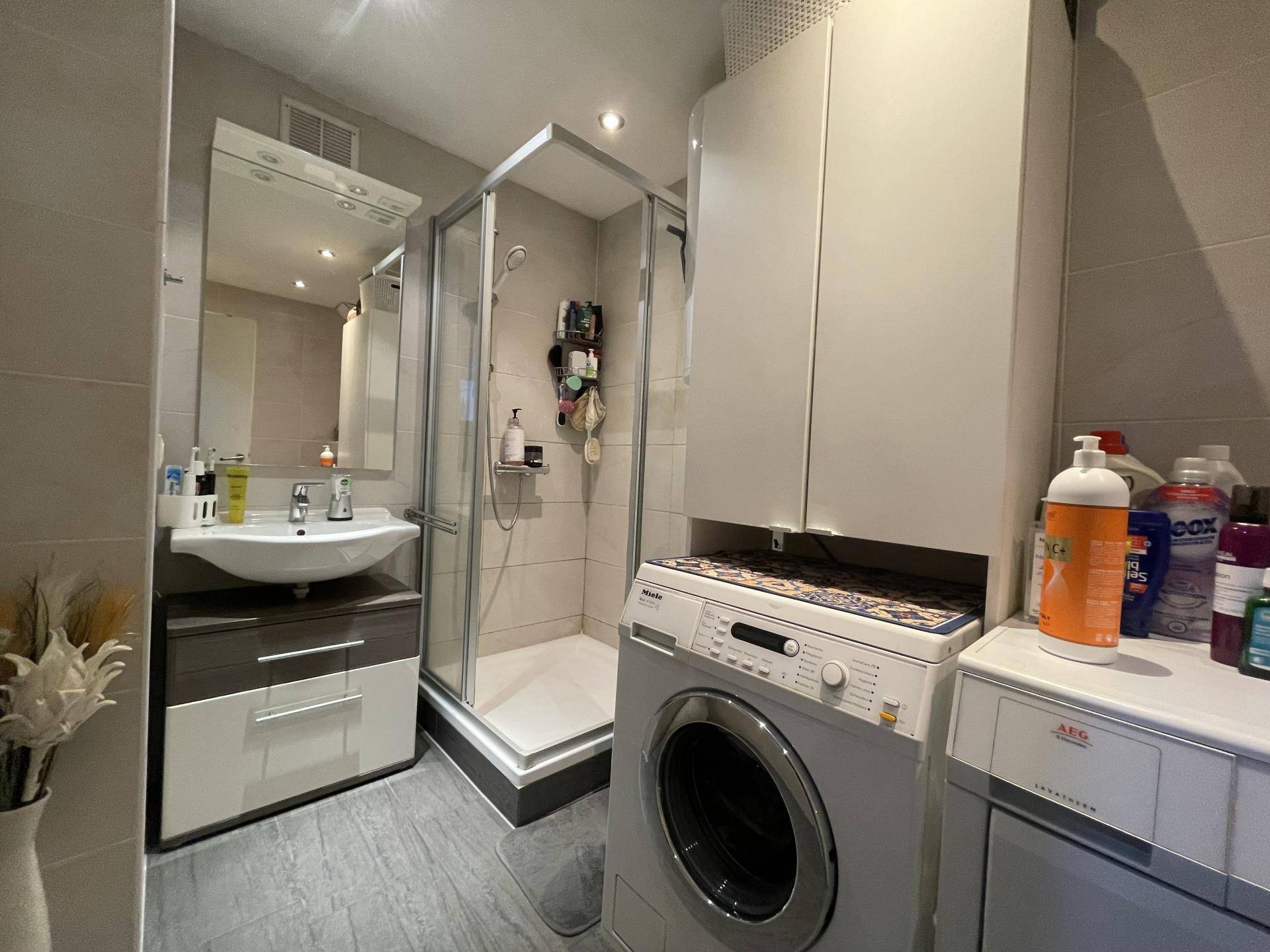 Modernes Badezimmer mit Duschkabine, Waschbecken und integrierter Waschmaschine.