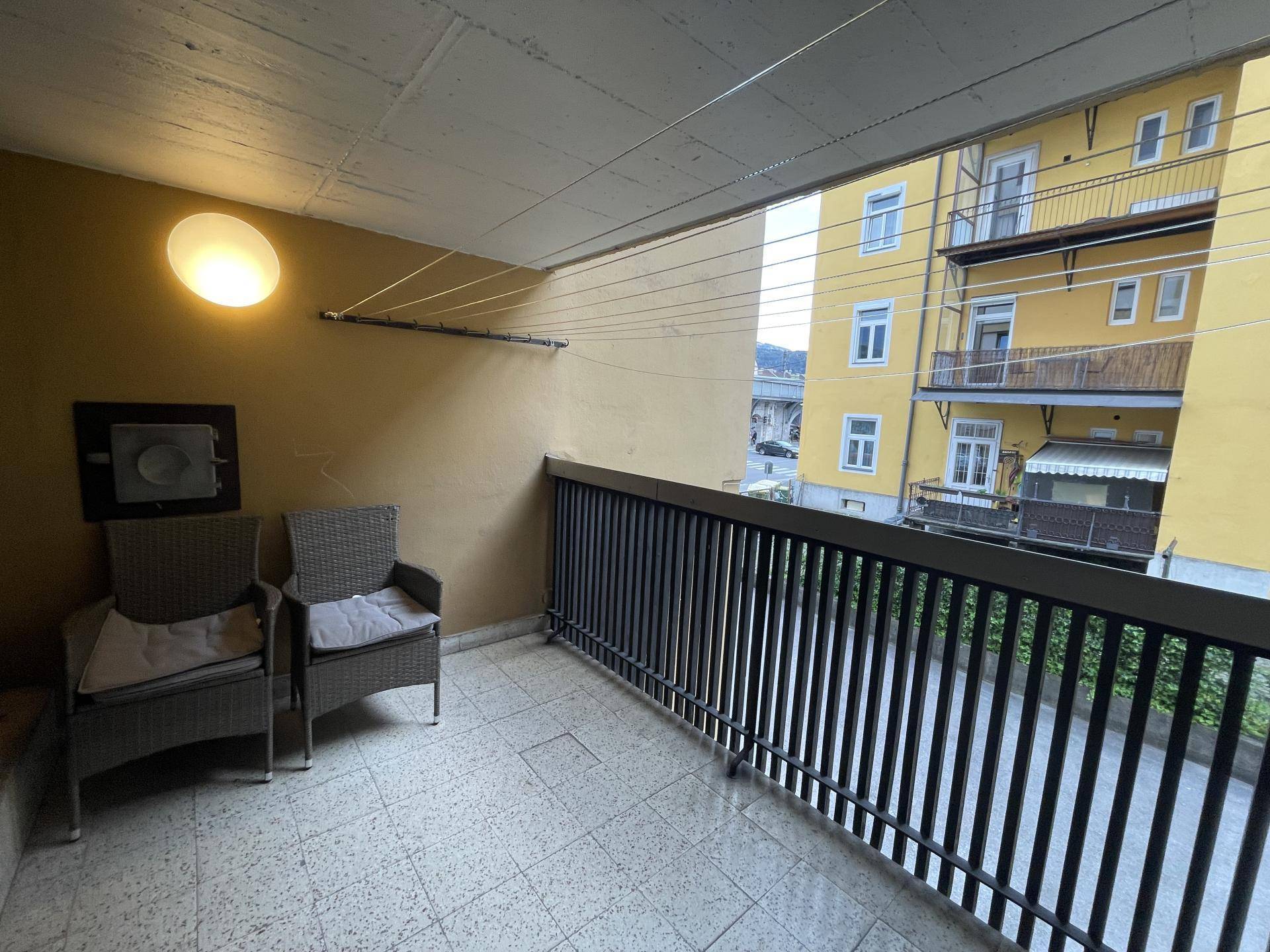 Überdachter Balkon mit Fliesenboden und Sitzgelegenheiten, mit Blick auf Nachbargebäude.