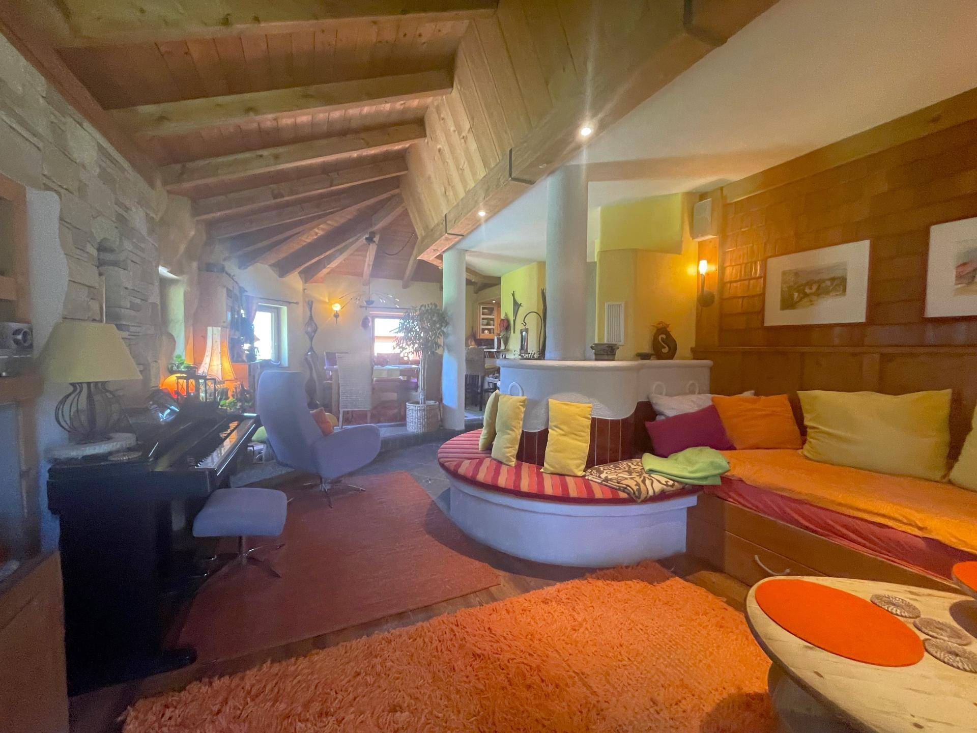 Geräumiges Wohnzimmer mit Holzbalkendecke, Steinwand, Klavier und gemütlicher Sitzecke.