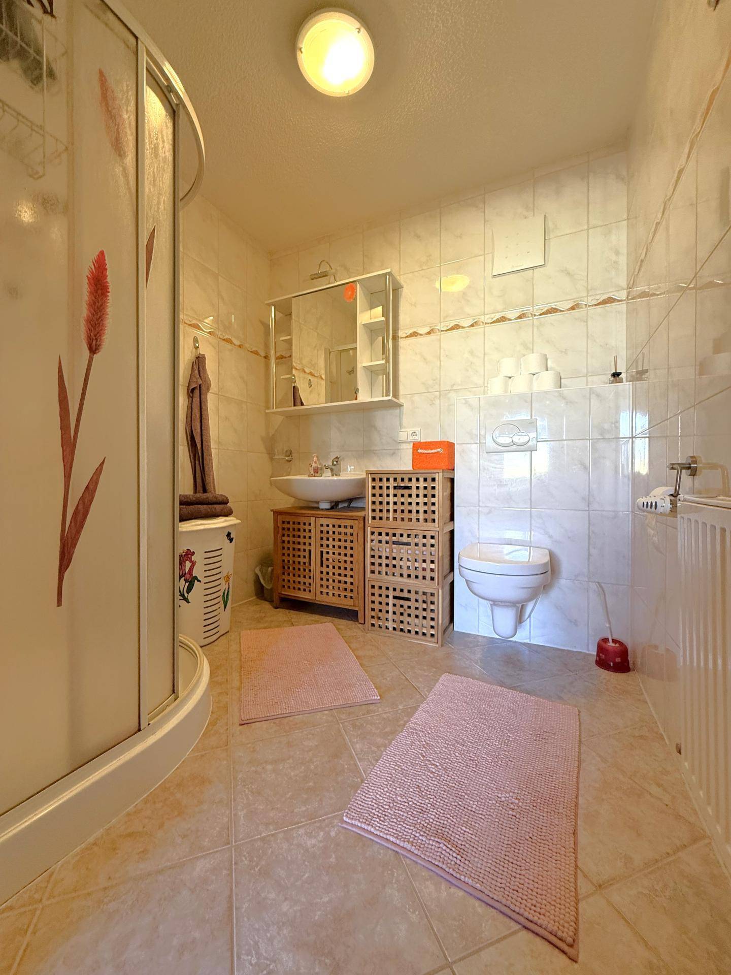 Helles Badezimmer mit Dusche, WC und Waschbecken, ausgestattet mit hellen Fliesen und Holzmöbeln.