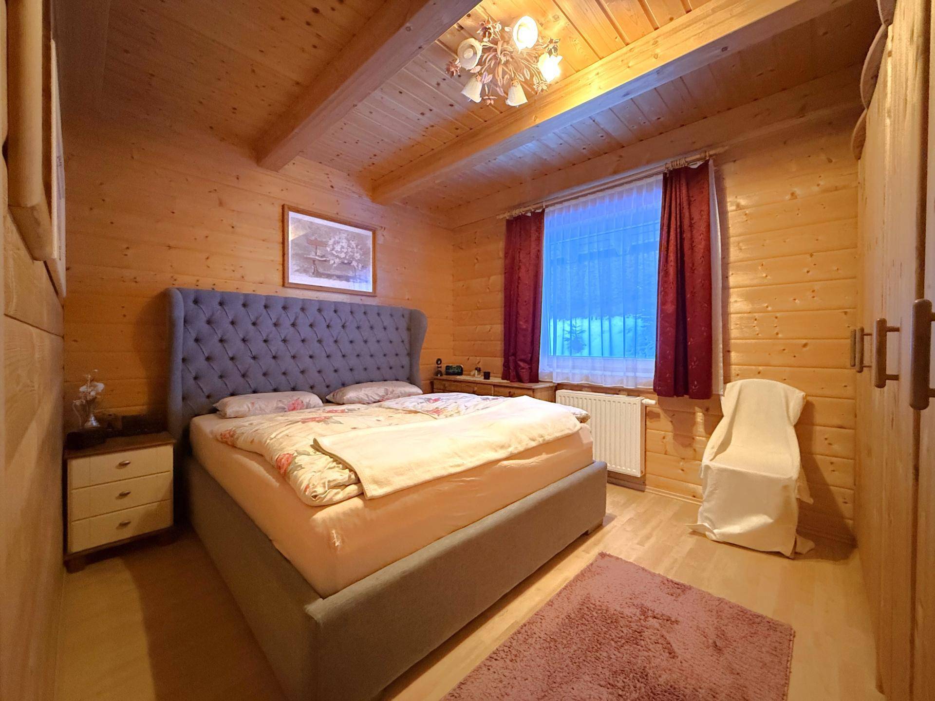 Schlafzimmer im Landhausstil mit Holzwänden, Doppelbett und Holzbalkendecke.