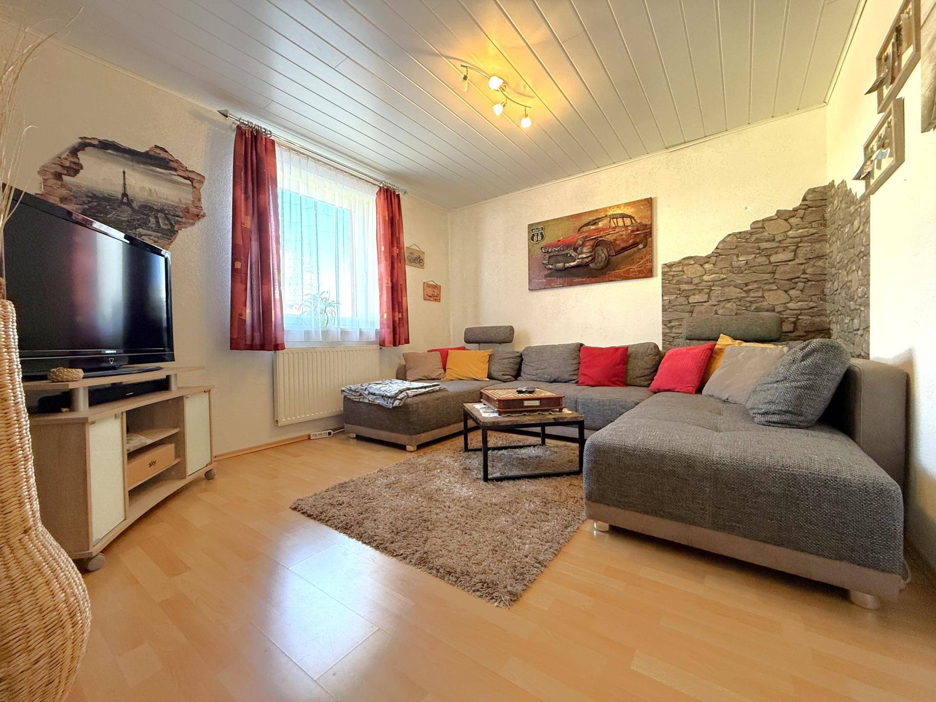 Gemütliches Wohnzimmer mit Laminatboden, großem Ecksofa und dekorativer Steinwand.
