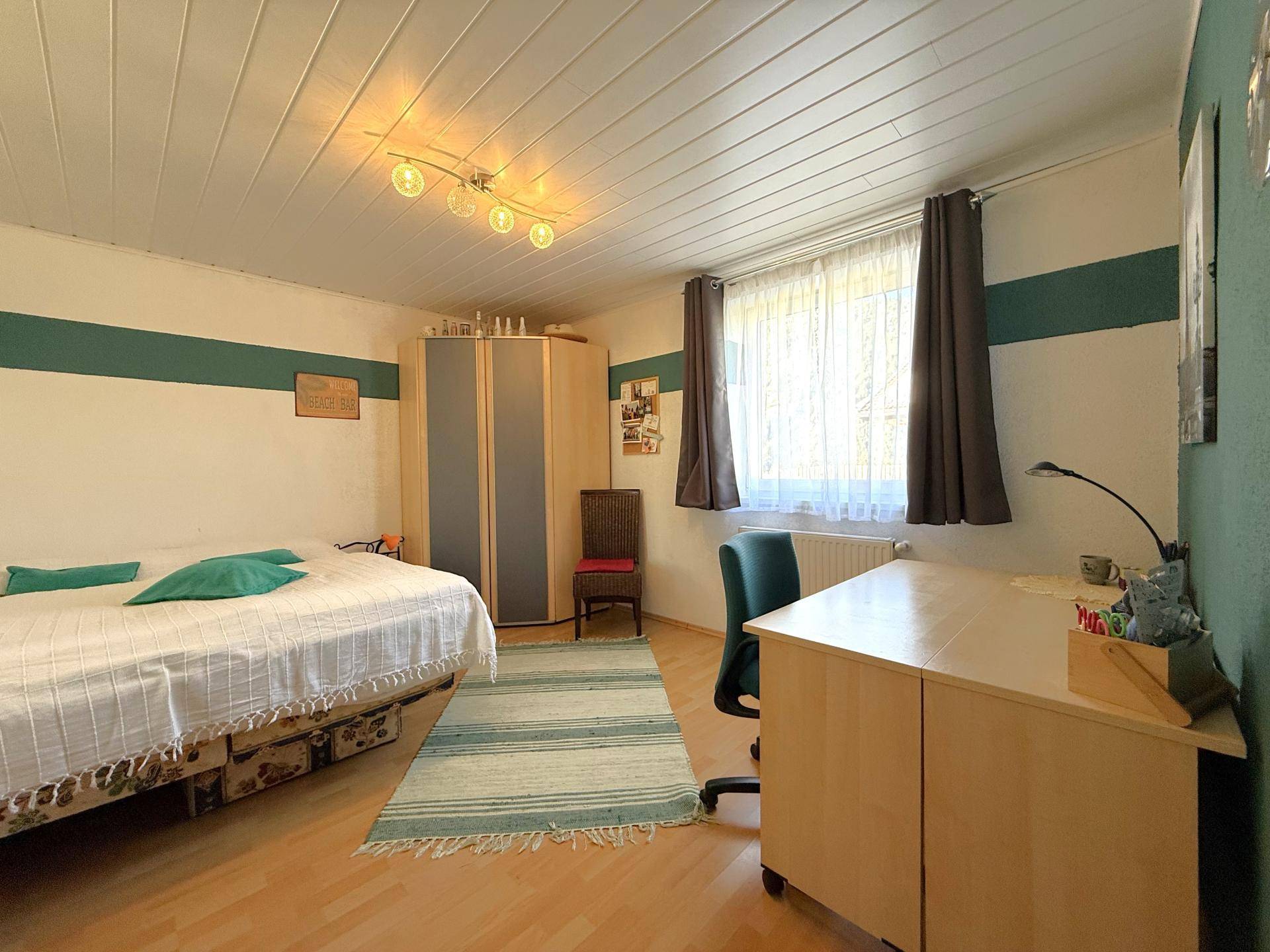 Helles Schlafzimmer mit Laminatboden, Kleiderschrank und Schreibtisch, ideal für Kinder oder Gäste.
