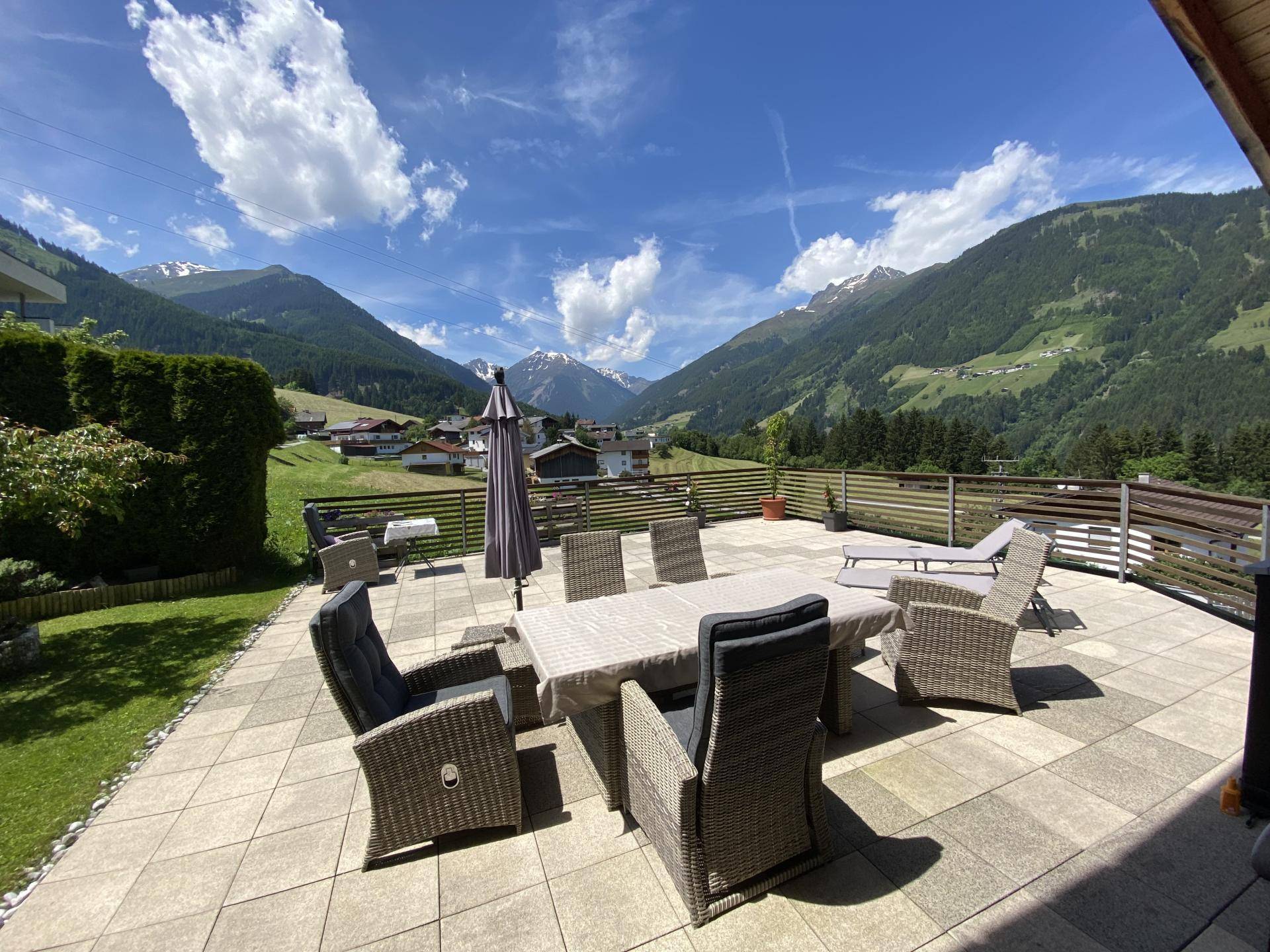 Große geflieste Terrasse mit Esstisch und Liegestühlen, umgeben von einer beeindruckenden Berglandschaft.